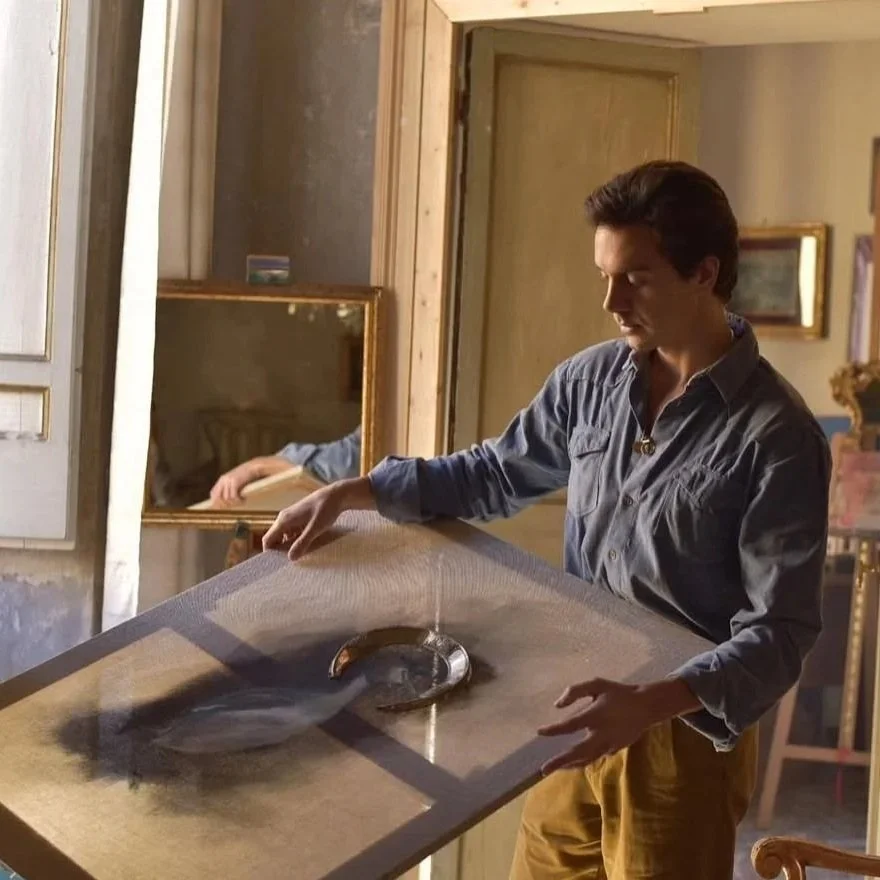 Joven sosteniendo un cuadro en una habitación decorada con espejos y cuadros en las paredes.