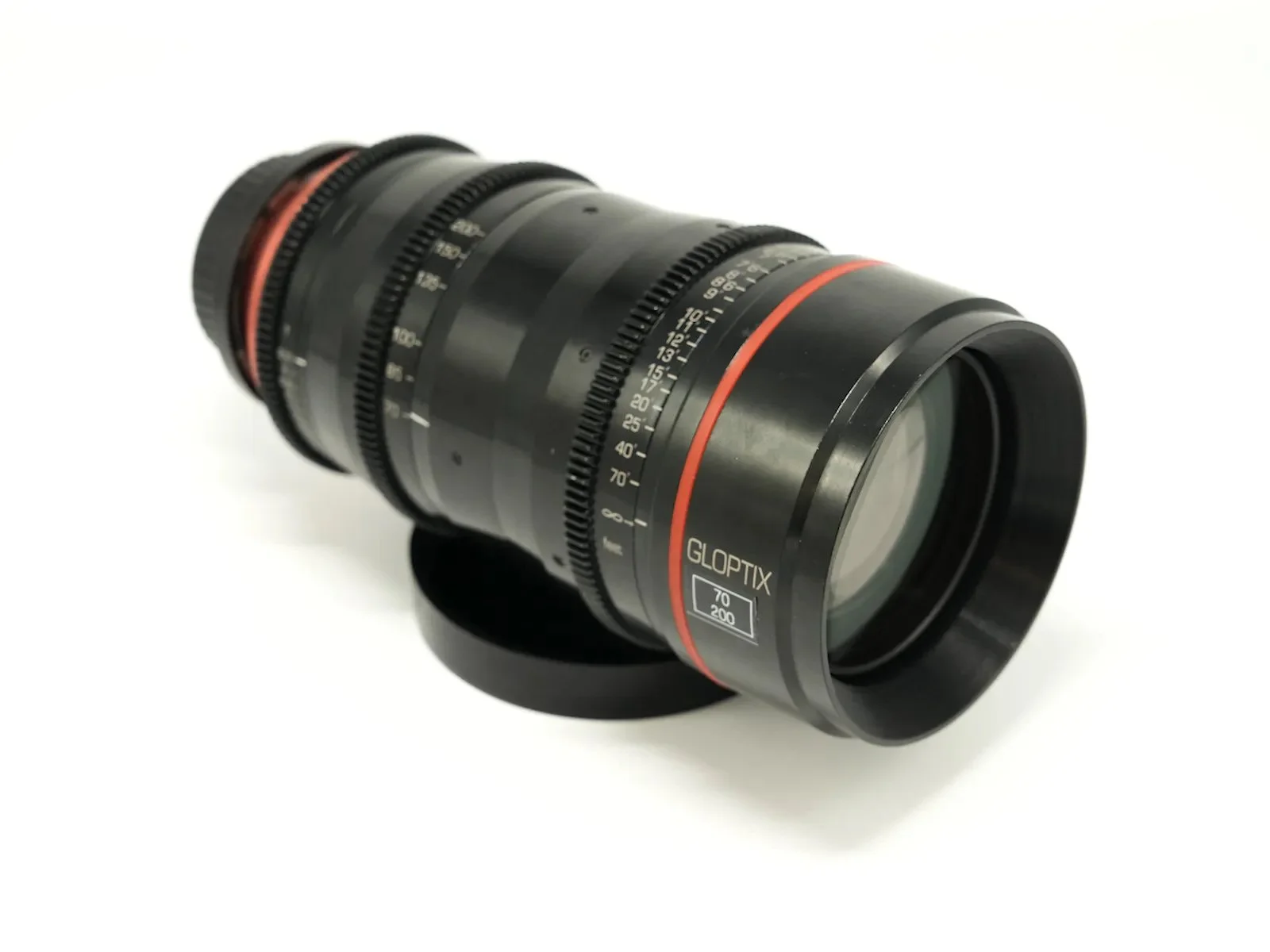 A professional camera lens with GLOPTIX branding, black with red accents, lying on a white surface.
