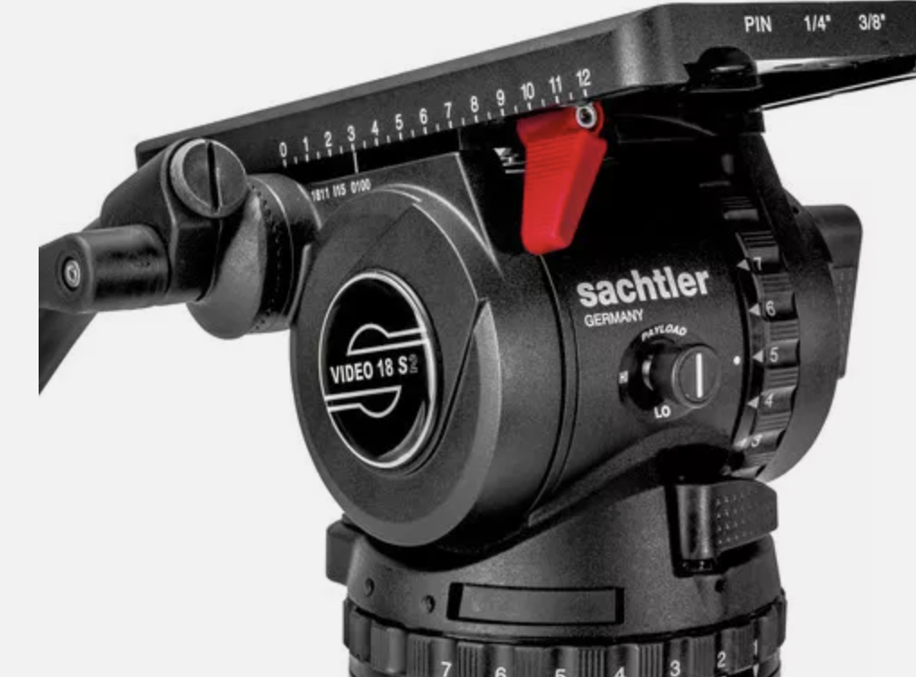 Close-up of a black Sachtler video camera tripod head with adjustment knobs and a red locking lever.