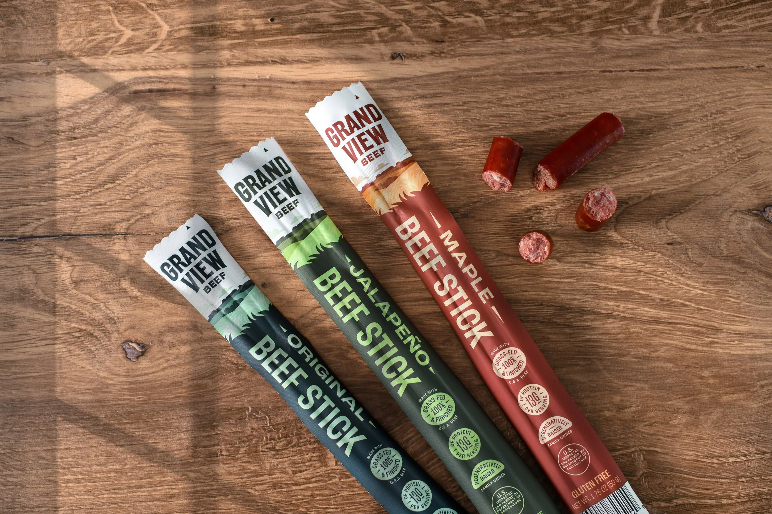 three beef sticks in thoughtfully designed packaging on a wood grain surface
