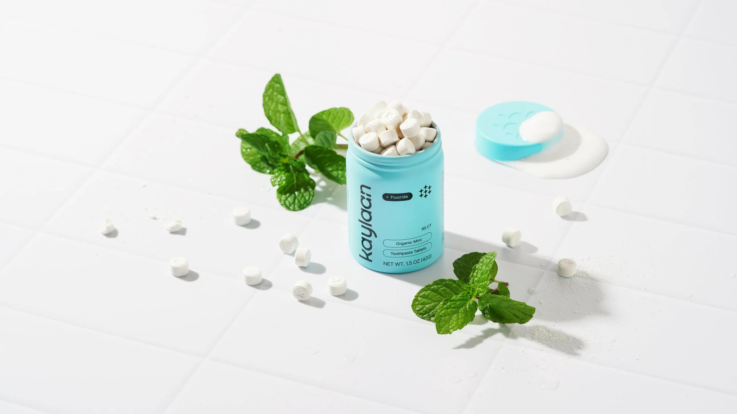 Kaylaan toothpaste tablets in a blue tin with tablets all around and mint leaves