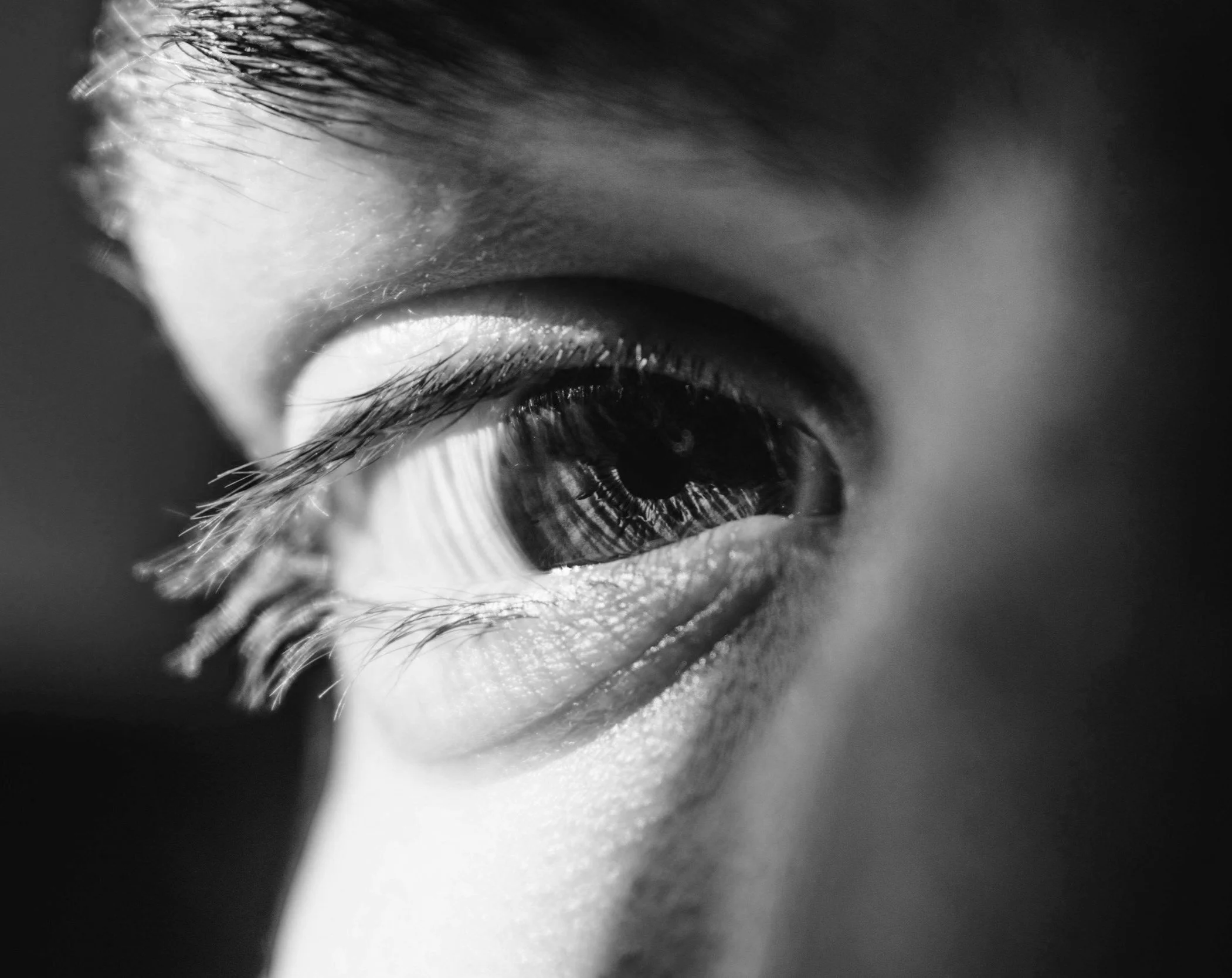 Gros plan d'un œil humain, en noir et blanc, avec détails des cils et de la peau autour.