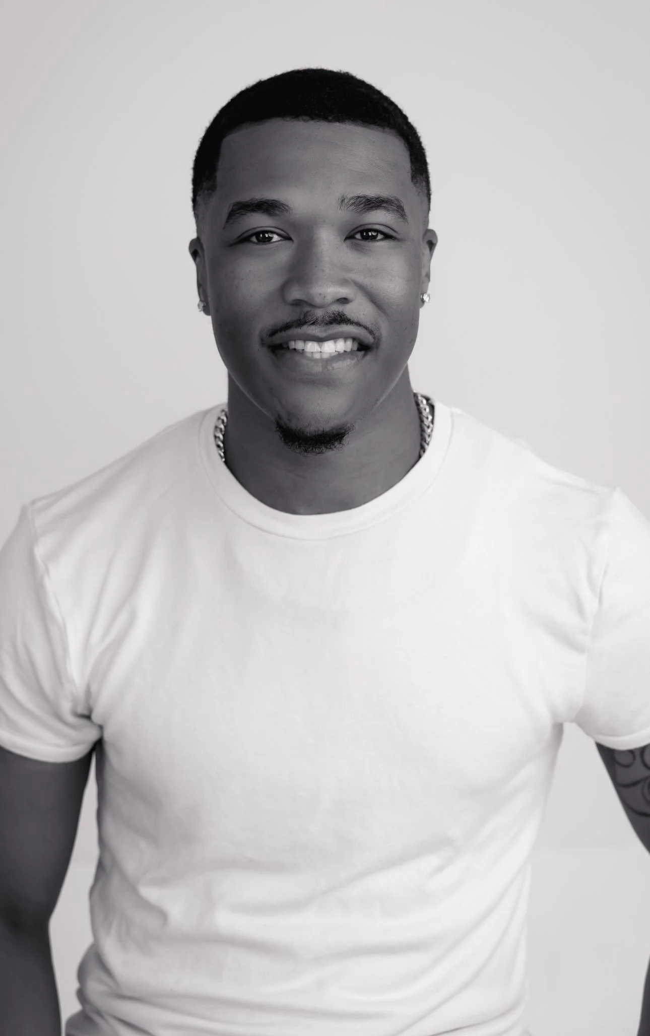 Black and white portrait of a smiling man in a white t-shirt with short hair and earrings.