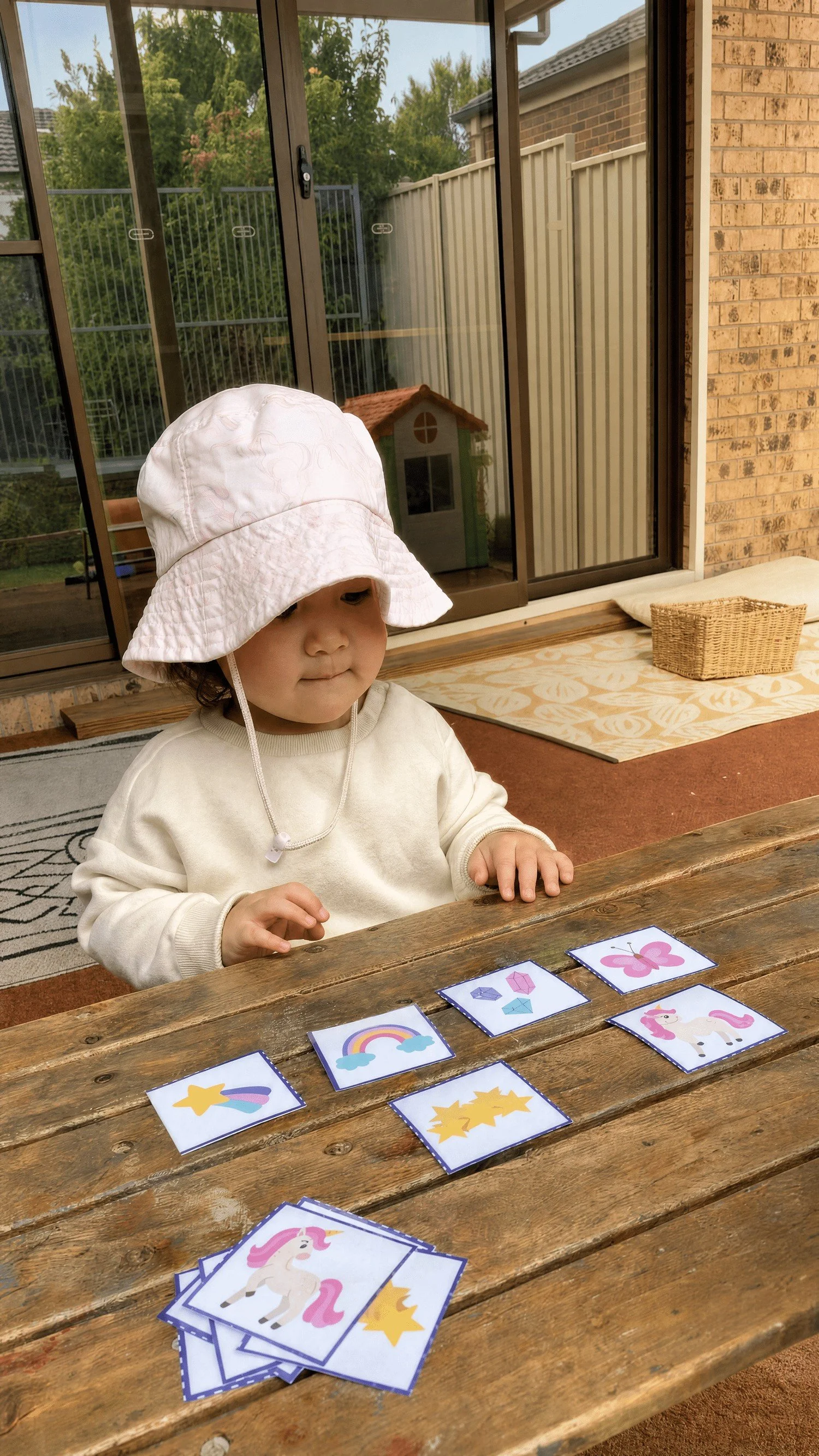 Toddler in a sun hat playing a matching card game outdoors
