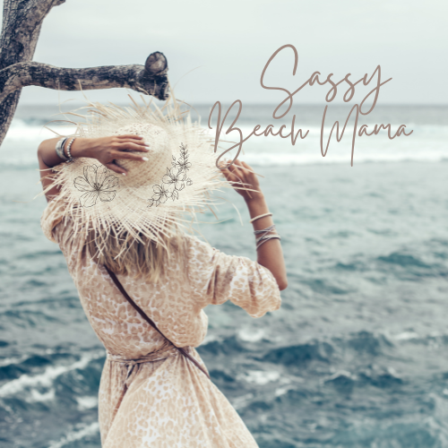 A woman with long blonde hair wearing a beige dress and a wide-brimmed hat decorated with floral embroidery, standing on a beach by the ocean and holding her hat with one hand, with her back to the camera. Text overlay reads "Sassy Beach Mama."