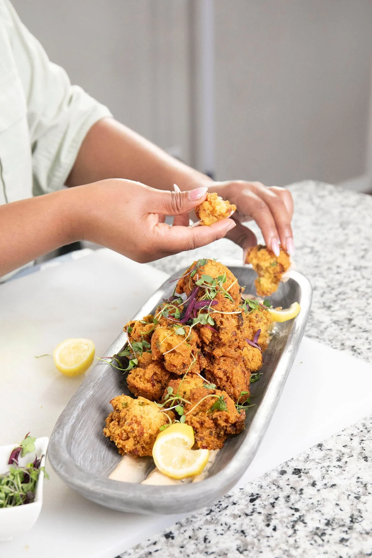 Person serving fried okra with lemon wedges on a tray on a granite countertop.