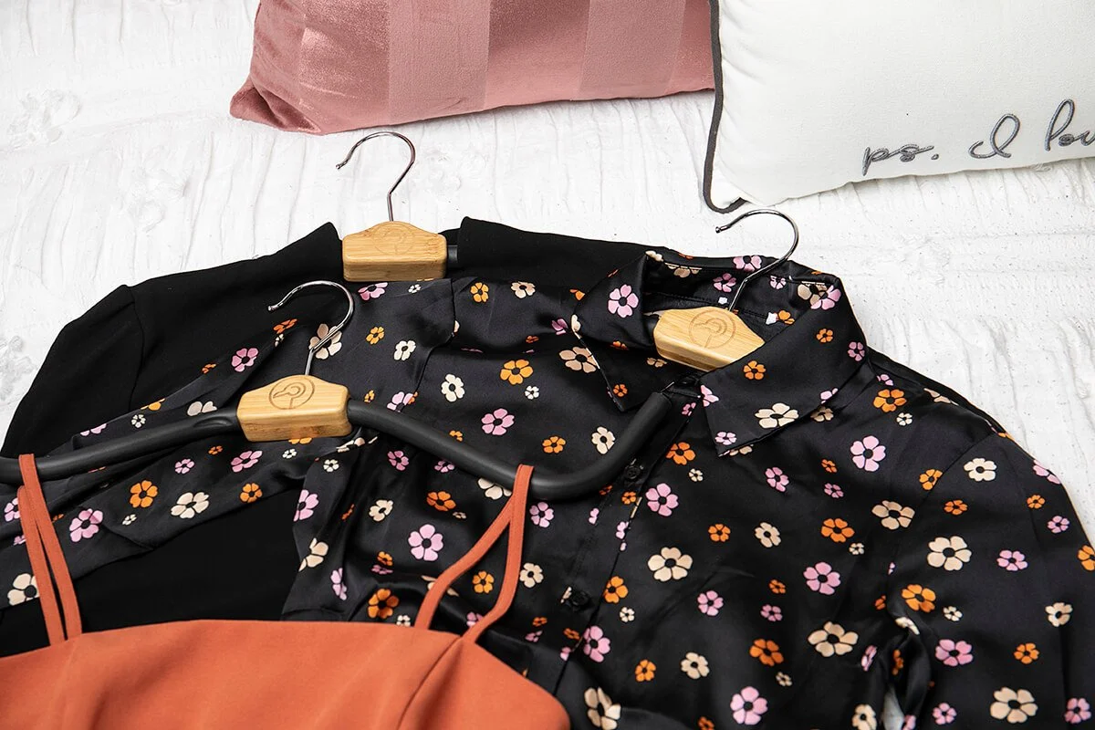 Floral patterned blouses on hangers with two pillows in the background.