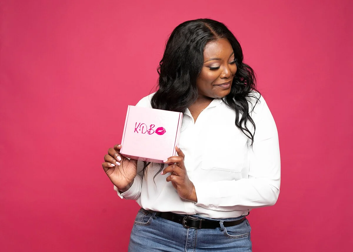 Woman in white shirt holding a pink box against a pink background.