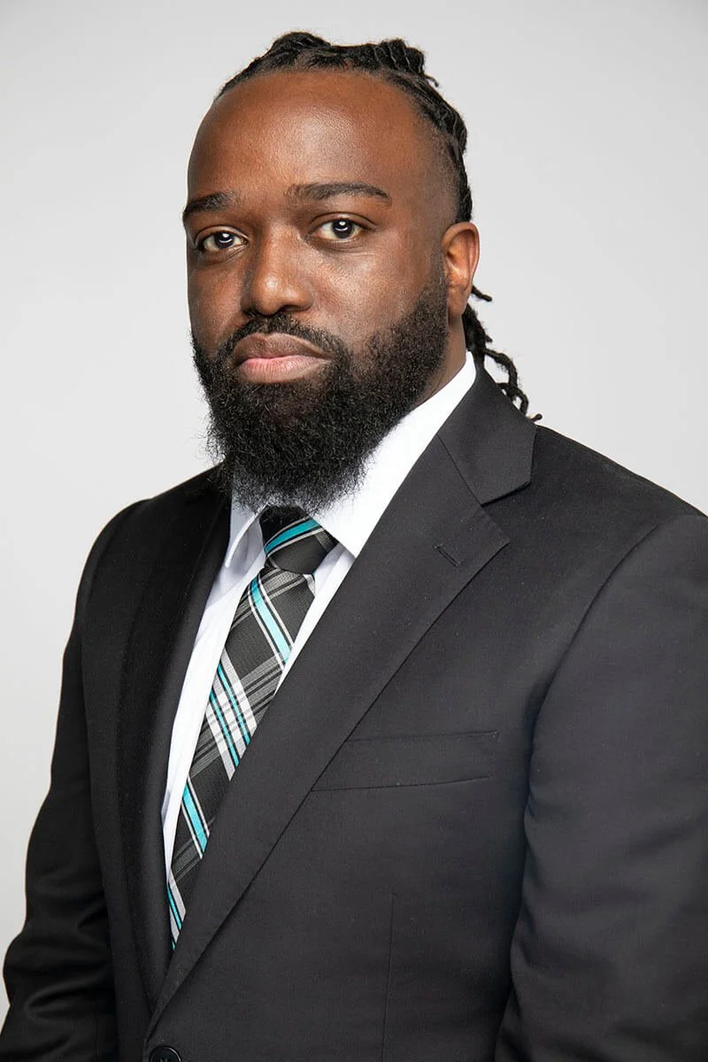 Man in black suit with white shirt and striped tie posing for a portrait