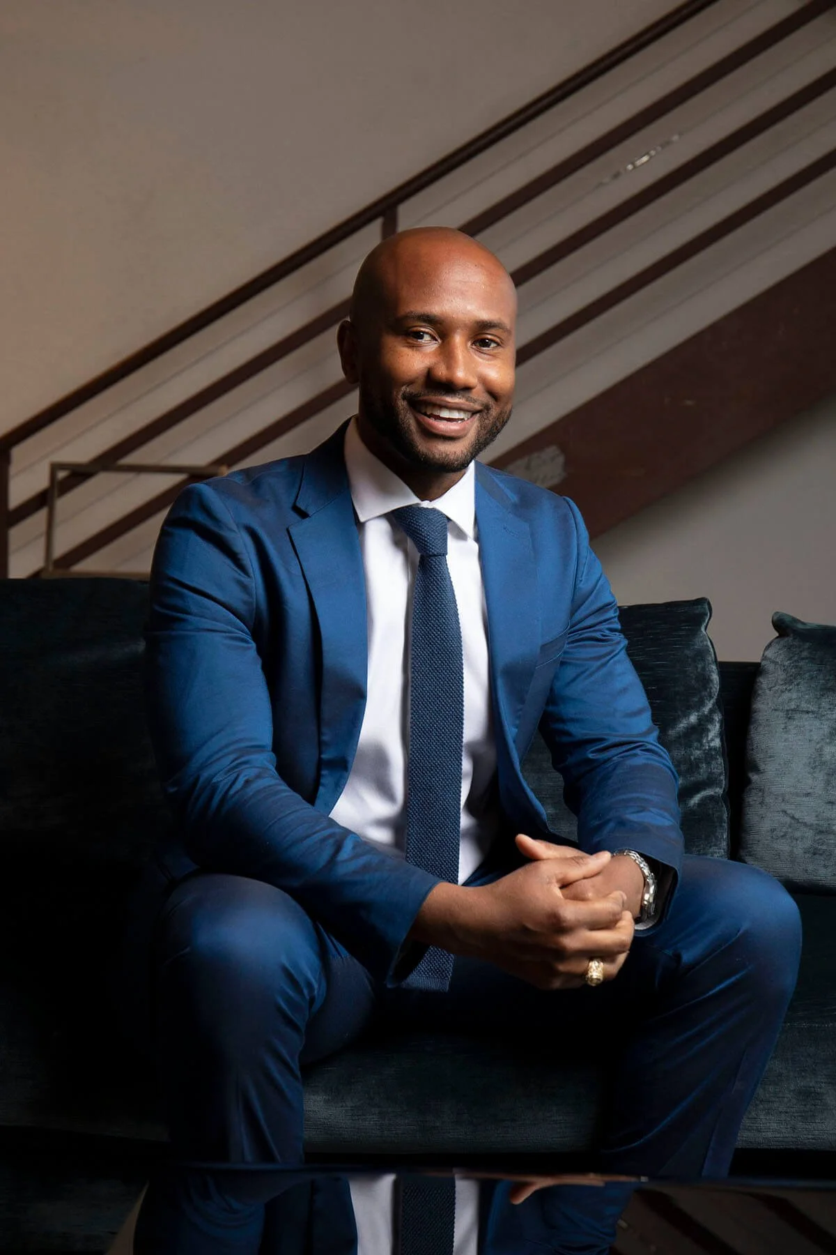 Smiling man in a blue suit sitting on a couch.