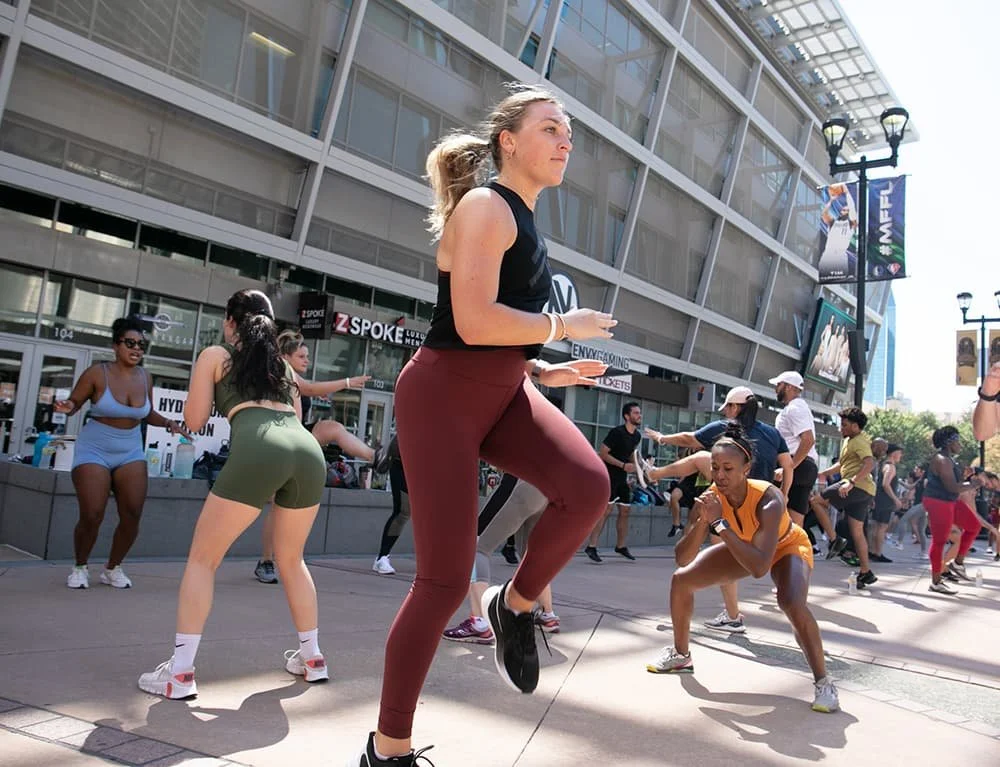 Group of people exercising outdoors in front of a modern building, participating in a workout class with various fitness activities.