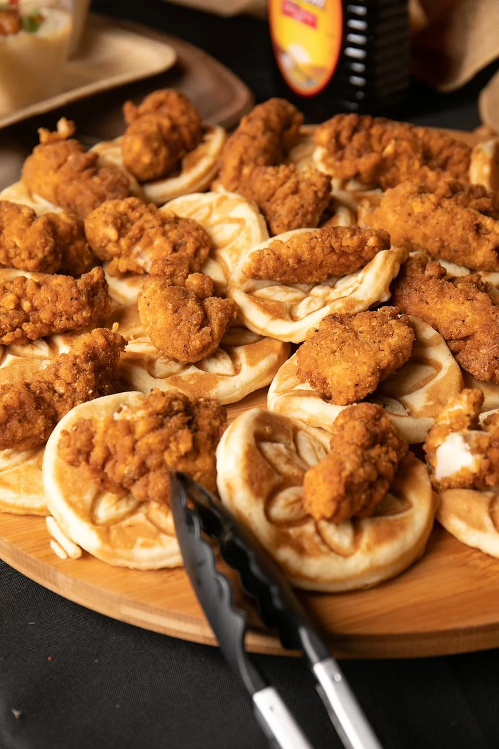 Chicken and waffles platter with syrup bottle and tongs