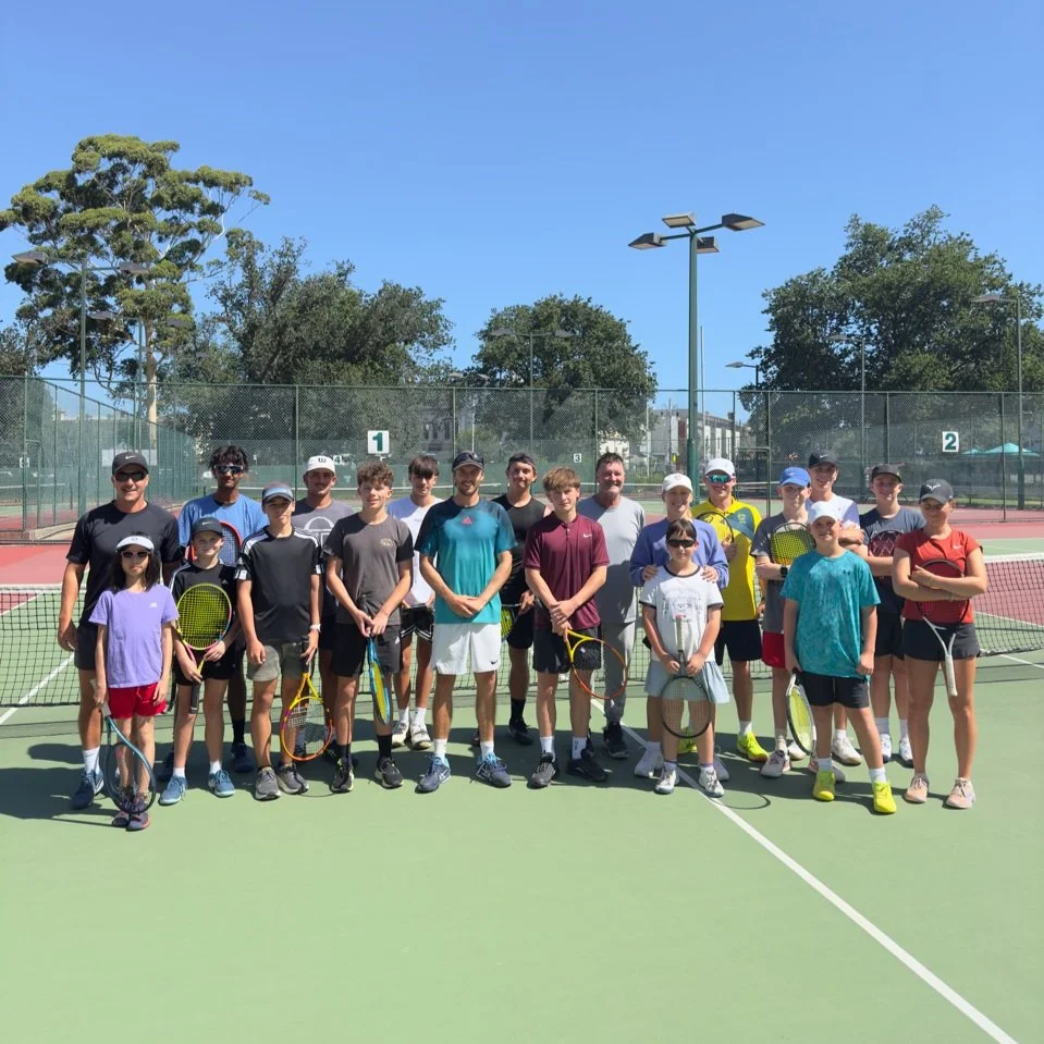Group of tennis players on an outdoor tennis court under a clear blue sky.