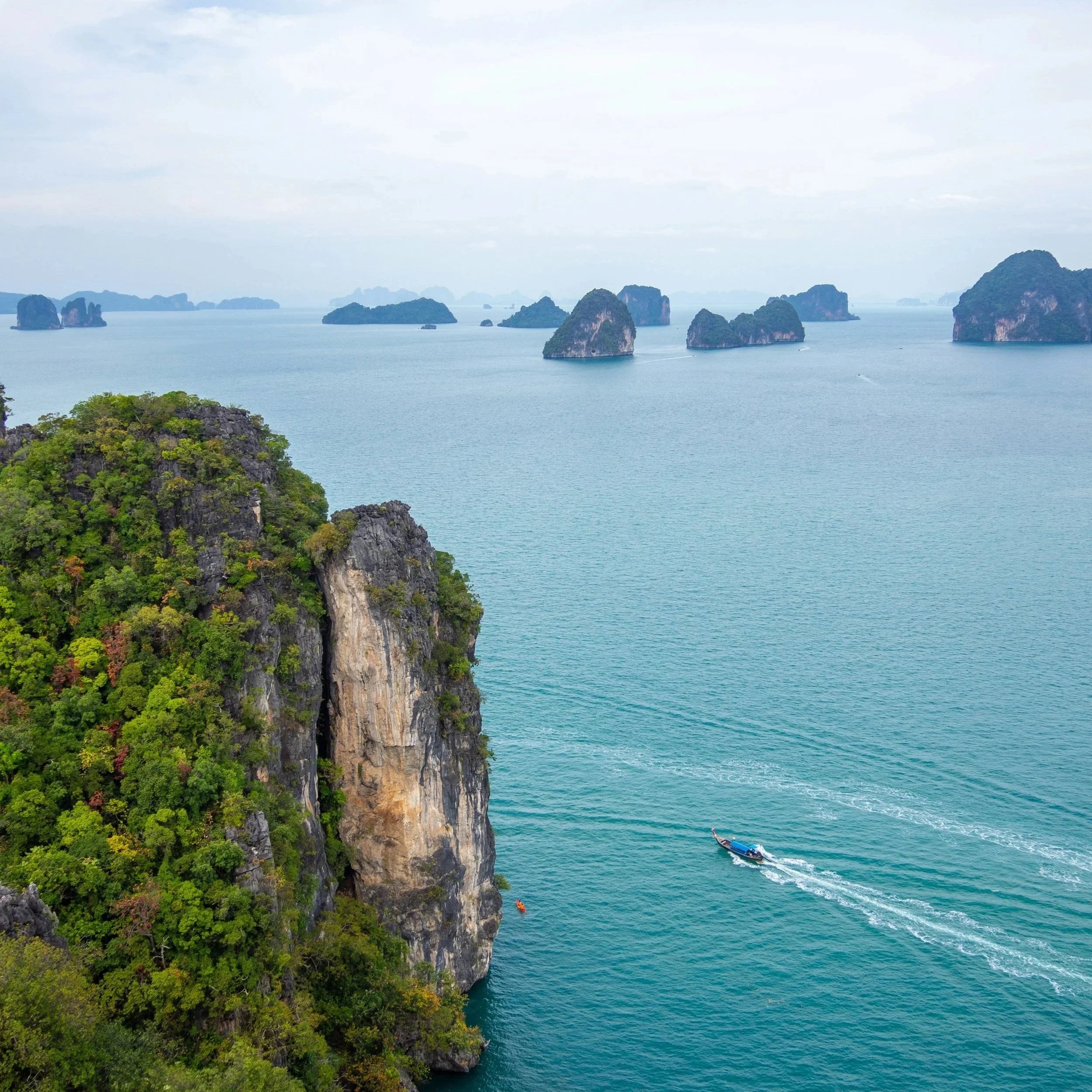 Limestone cliffs and islands in the Andaman Sea near Phuket, longtail boat cutting through calm turquoise water