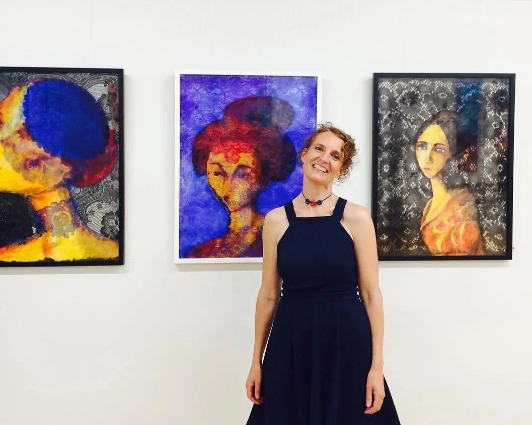 A woman in a black dress smiling at an art exhibition titled 'Her Colours' by Tamzin Blair, with three colorful paintings of women displayed on the wall behind her. Mira Corbova Art Gallery Sydney