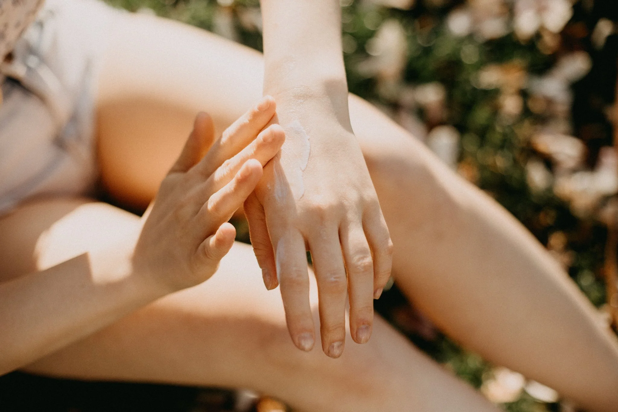 Person applying lotion or sunscreen to their hand outdoors, with blurred natural background.