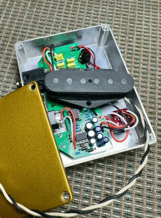 Inside view of an electronic guitar effects pedal or similar device with circuit boards, wires, and a black rubber pad, on a textured surface.