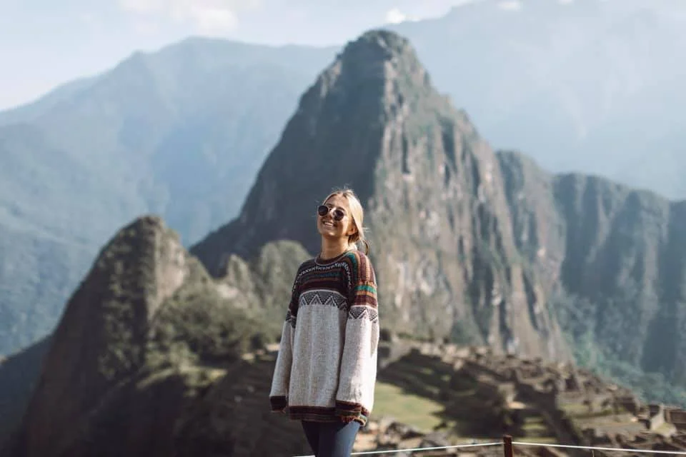 Smiling woman with sunglasses standing in front of Machu Picchu in Peru.