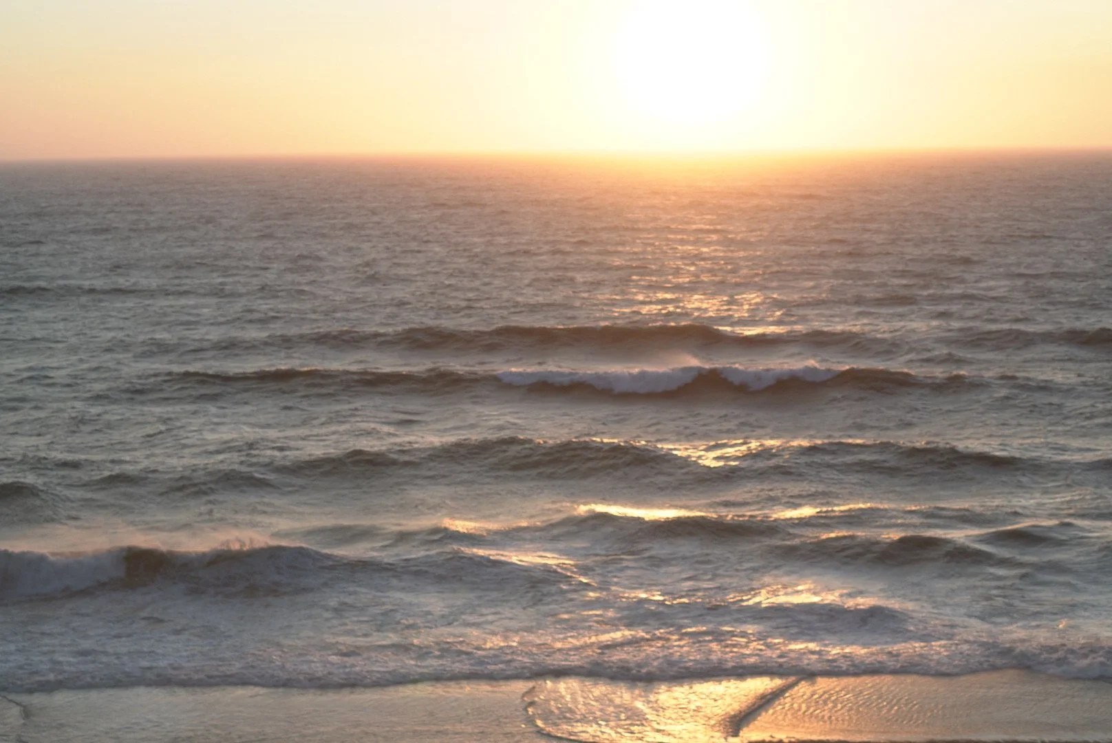 Sunset over the ocean with waves gently crashing onto the shore.