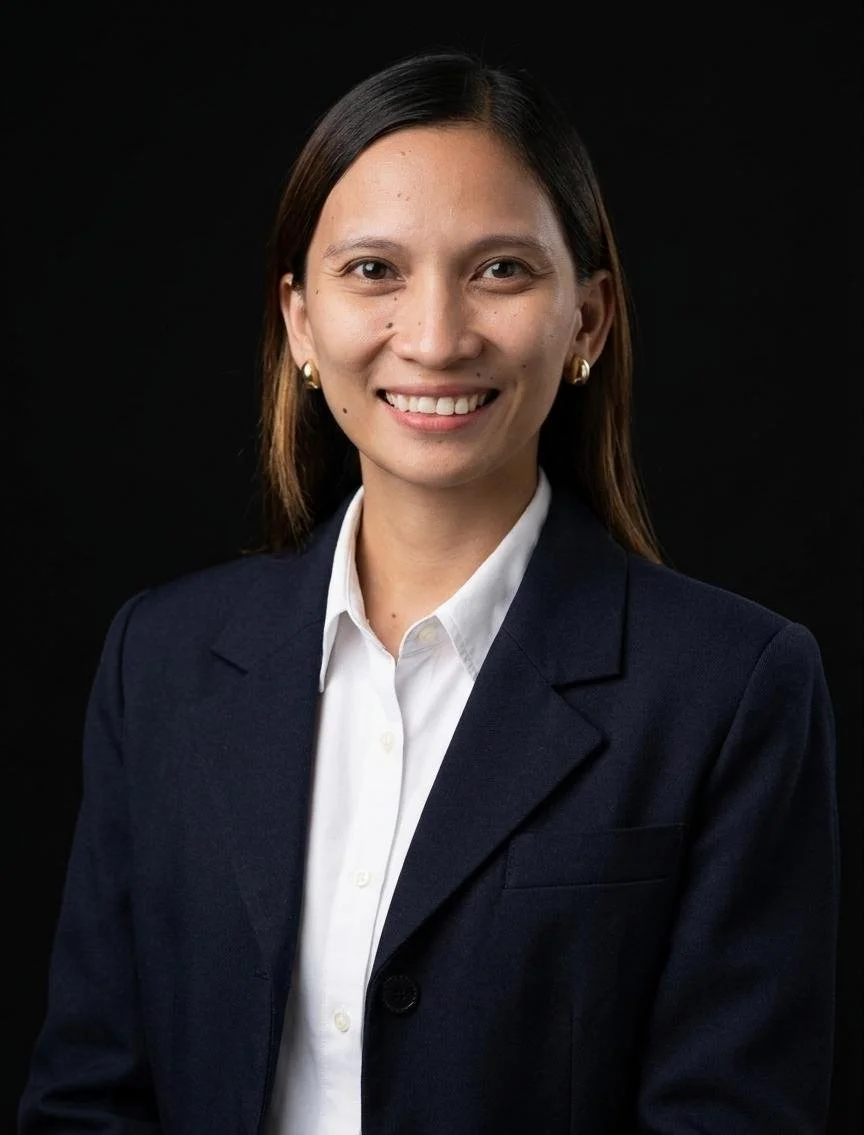 Portrait of a woman with long brown hair wearing a dark blazer and white shirt, smiling against a black background.