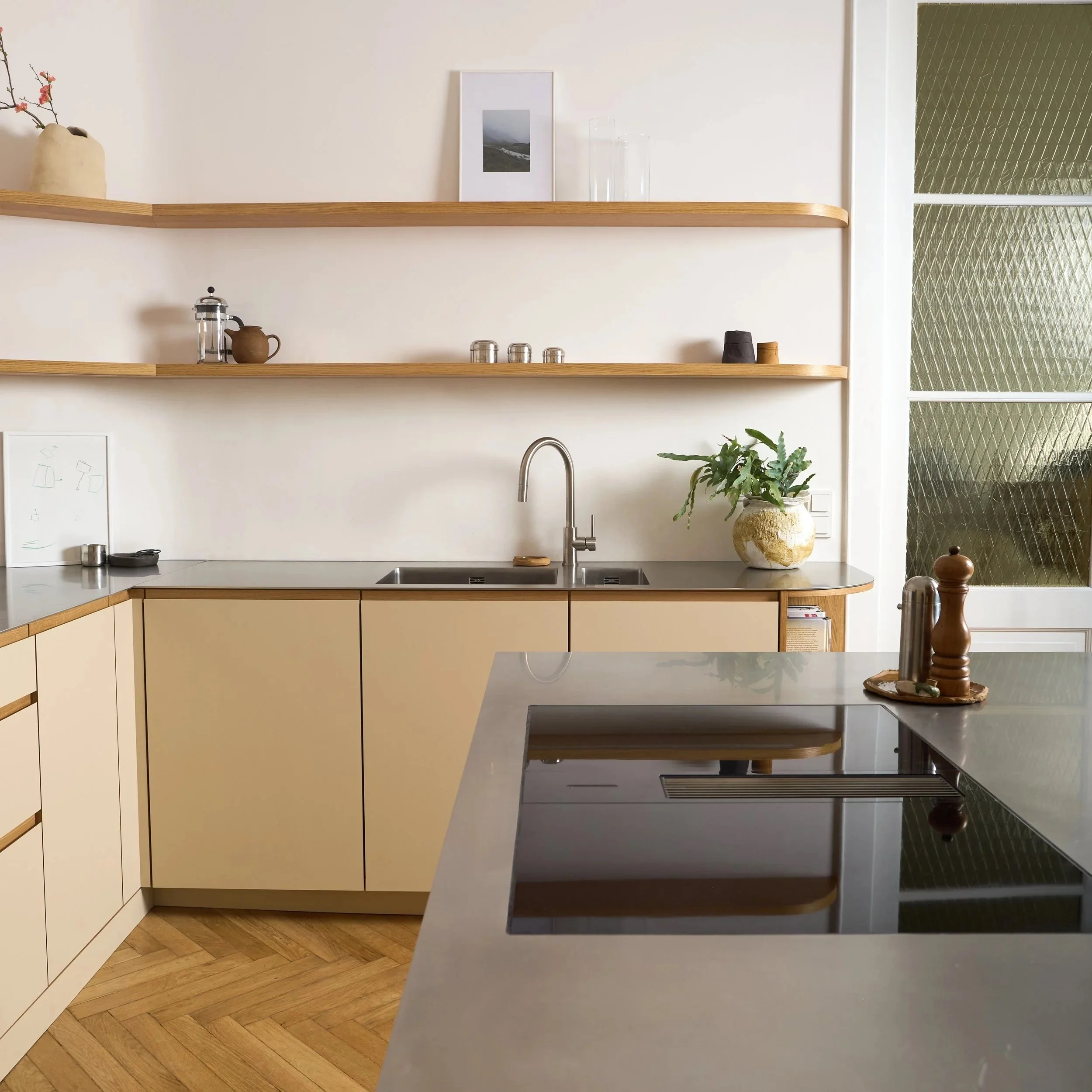 Moderne Küche mit beige Schränken, Edelstahlspüle, offenen Holzregal und grüner Pflanze in einer weißen Vase