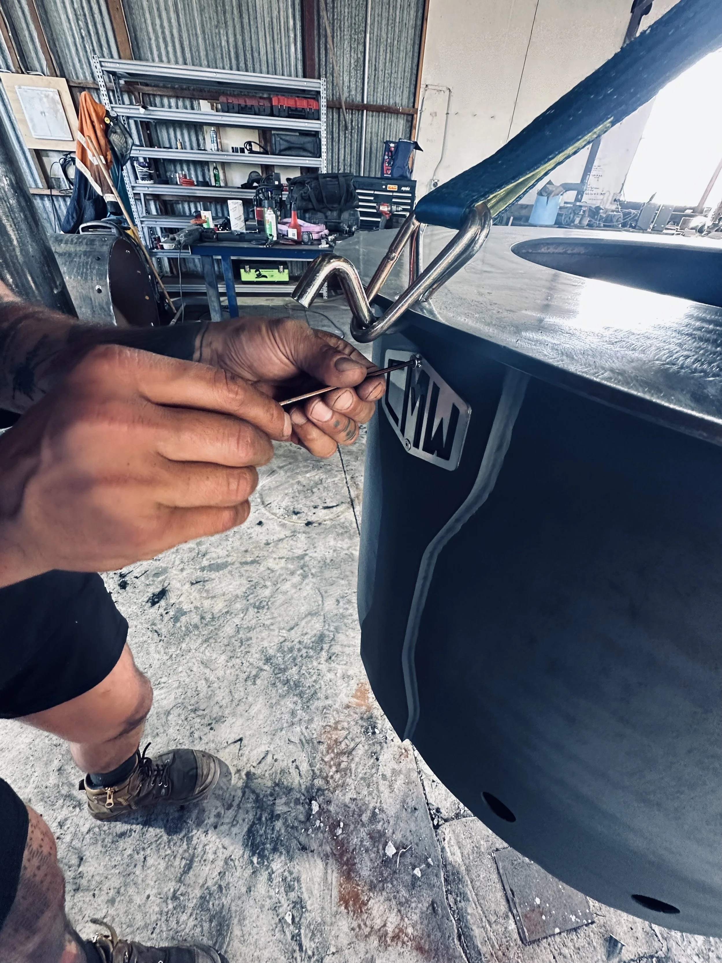 Close-up of hands adjusting a metal hook on a large industrial drum inside a workshop.