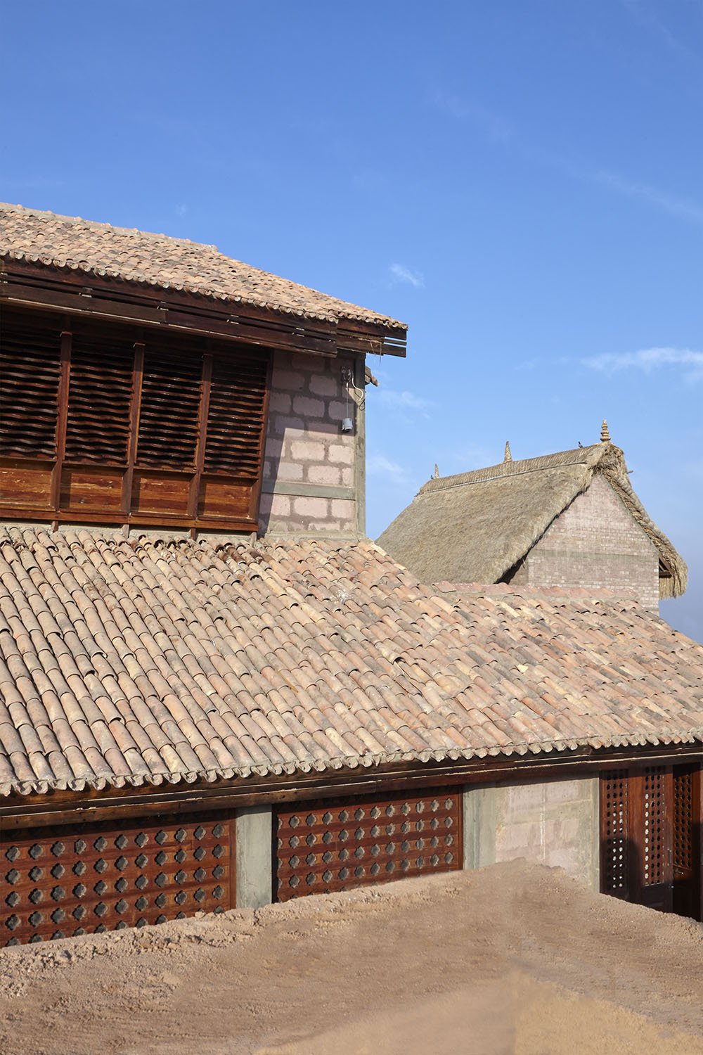Traditional thatched and tiled rooftops of Balinese houses under a blue sky.