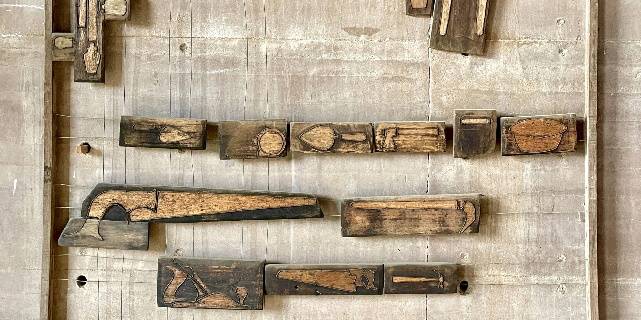 Wooden blocks arranged on a tiled floor, each with a metal outline of a different object or animal inscribed on the surface.