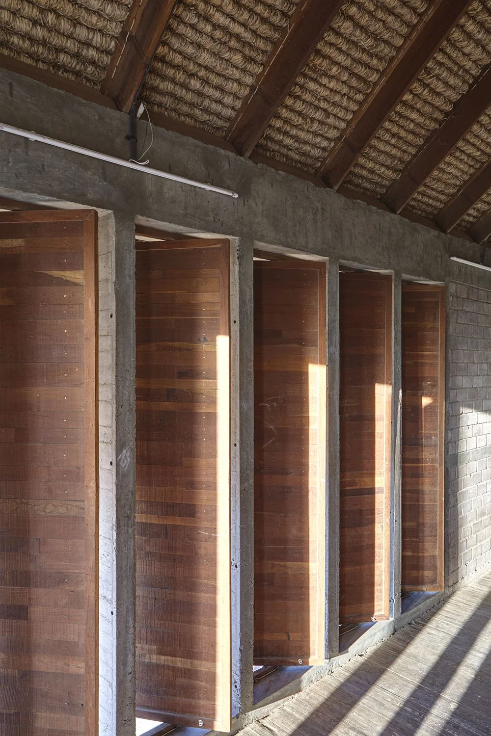Wooden shutters on a brick and concrete wall, with sunlight casting shadows on the floor.