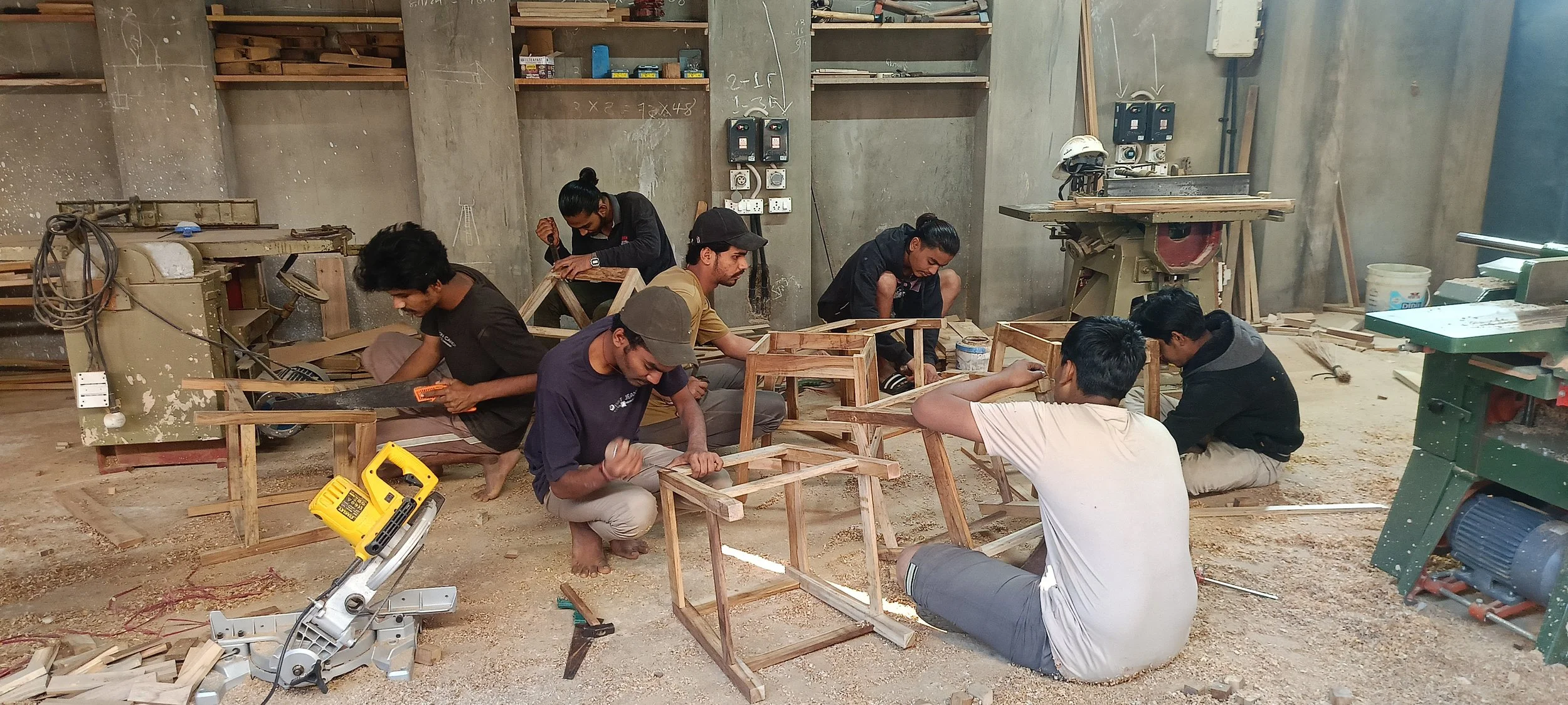 A group of young people working together in a woodworking workshop, assembling wooden furniture. They are using various tools and surrounded by woodworking equipment and materials.