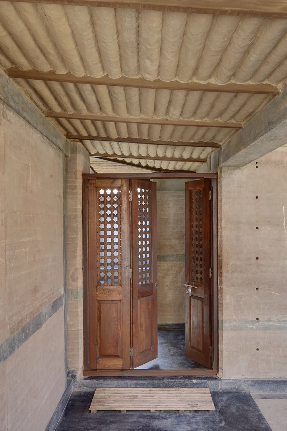 Open wooden lattice doors leading to a small room with unfinished brick walls and a corrugated ceiling.
