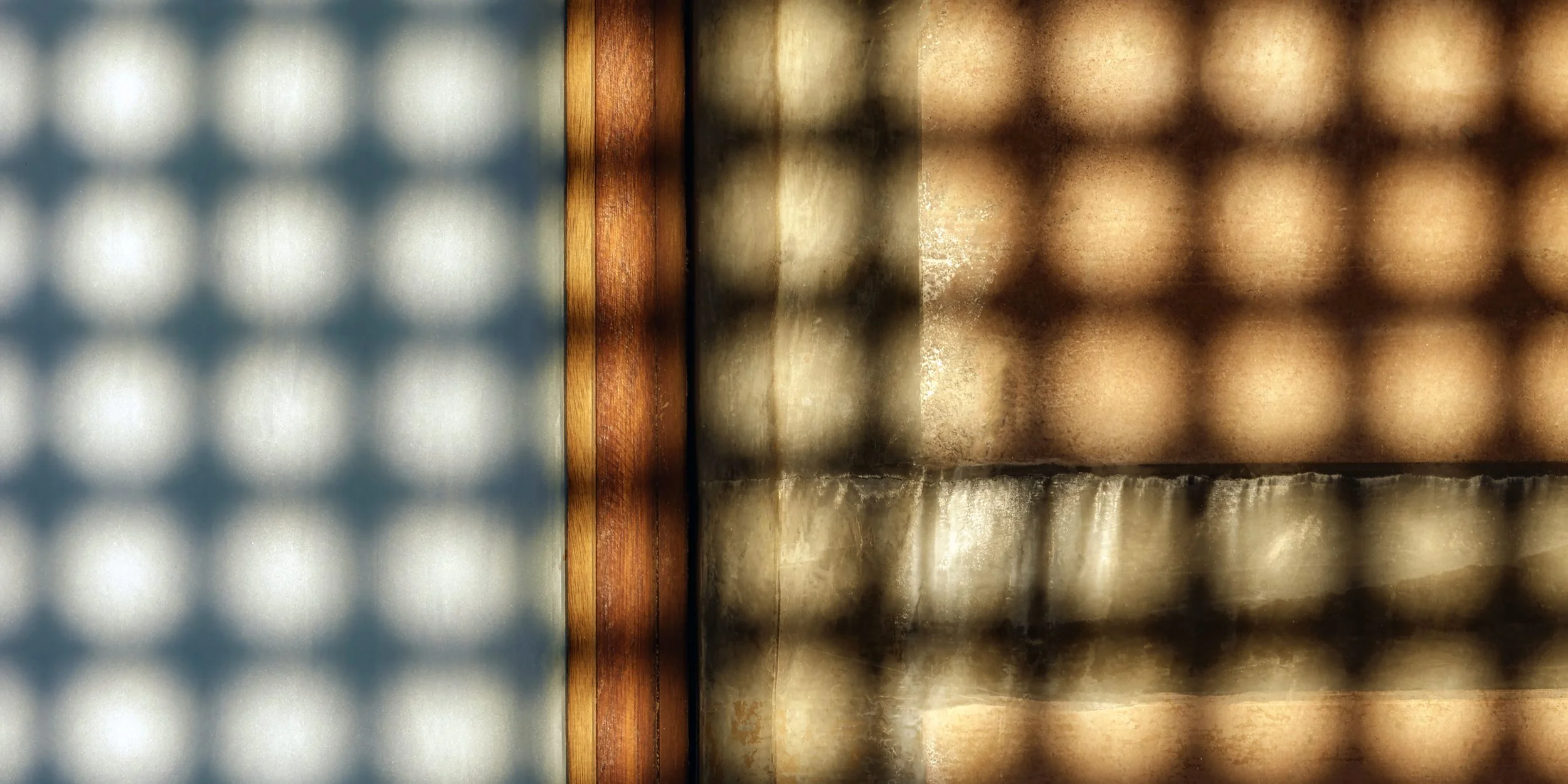 Close-up of two textured glass panels separated by a thin wooden strip, one panel has a bluish tint with a grid pattern, the other has a warm, brownish hue with a different pattern.