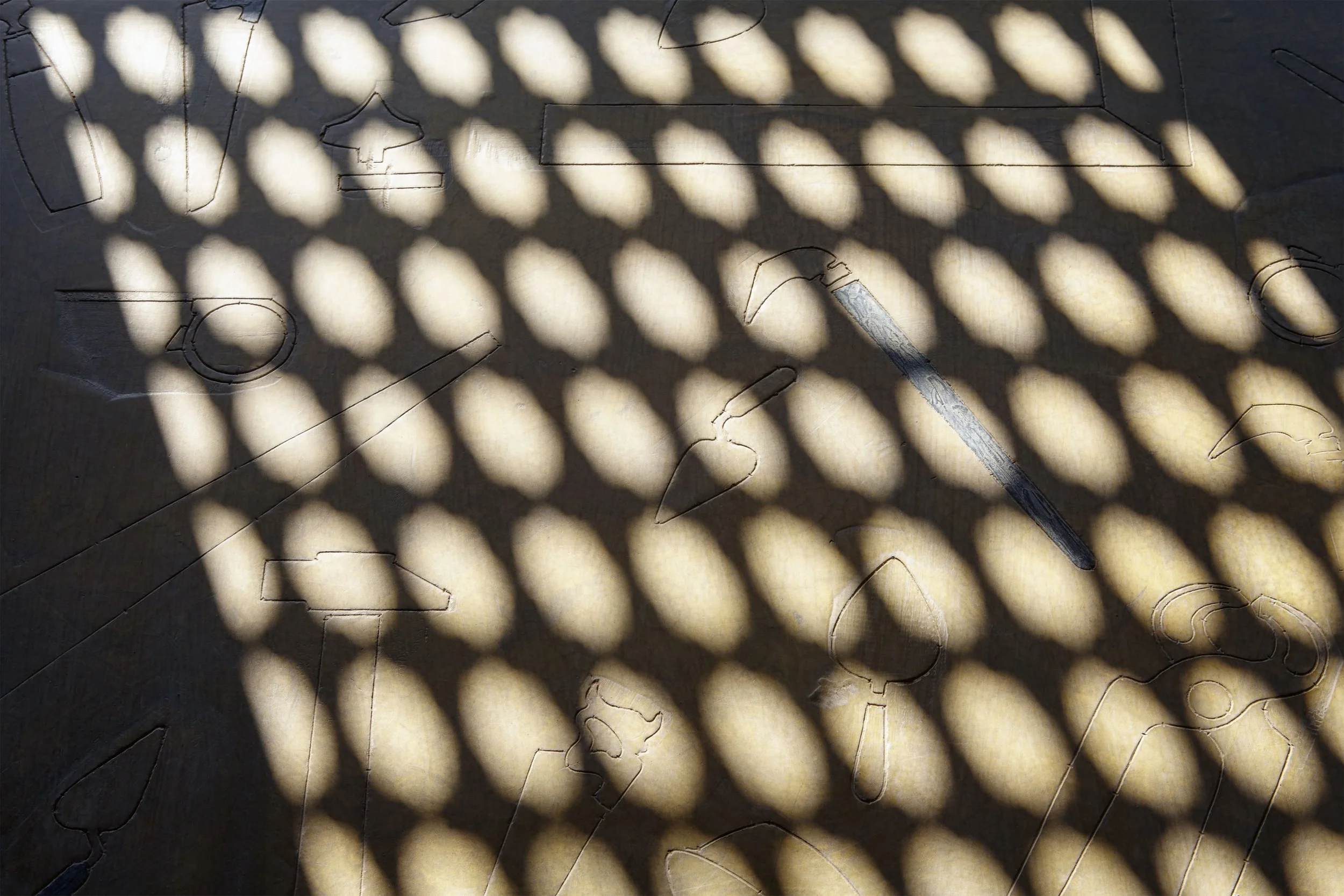 Shadow of a lattice pattern cast on a surface with scattered cut-out shapes and cracks.