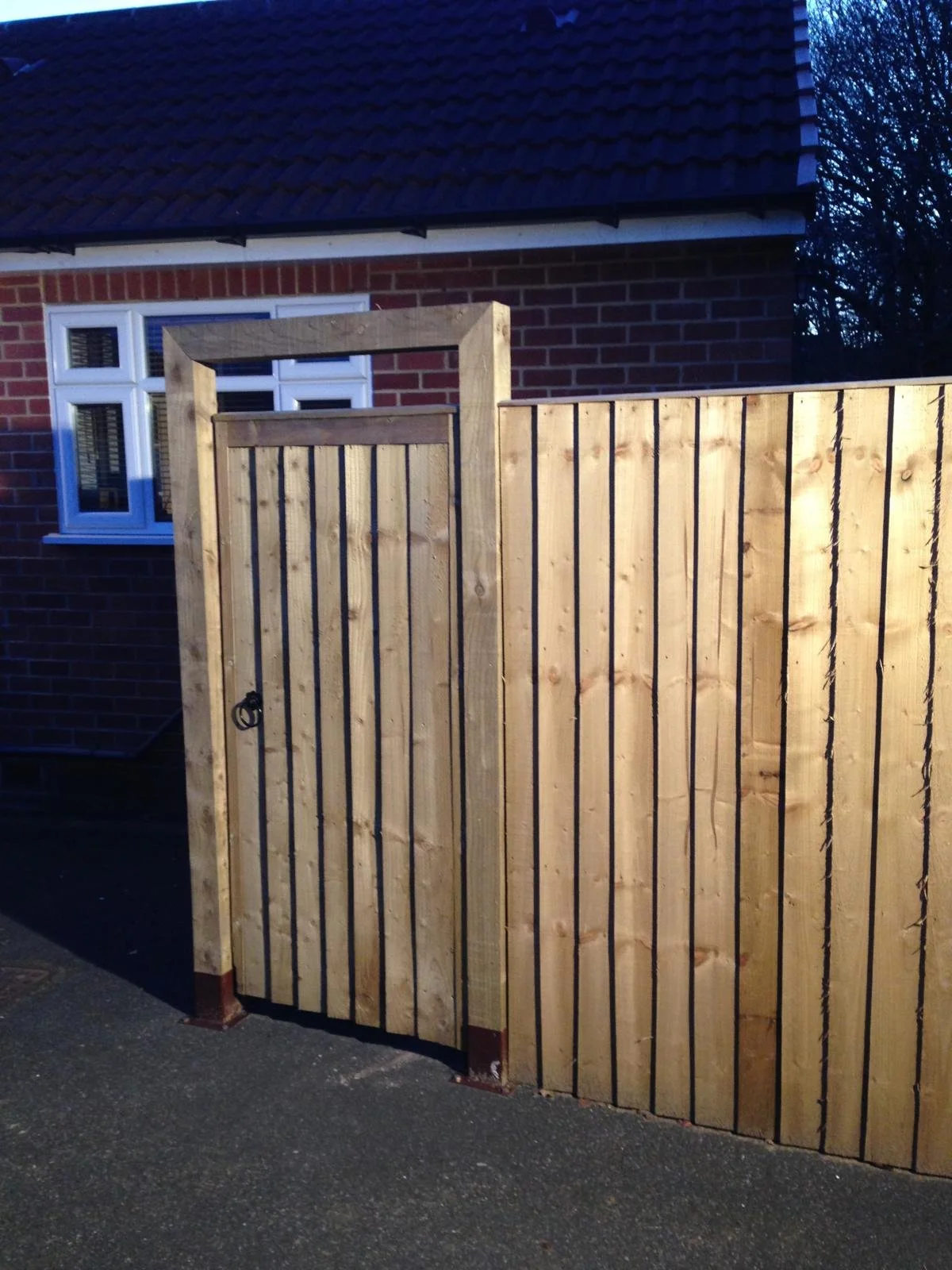 Newly constructed wooden fence and gate outside a brick house with white window frames.