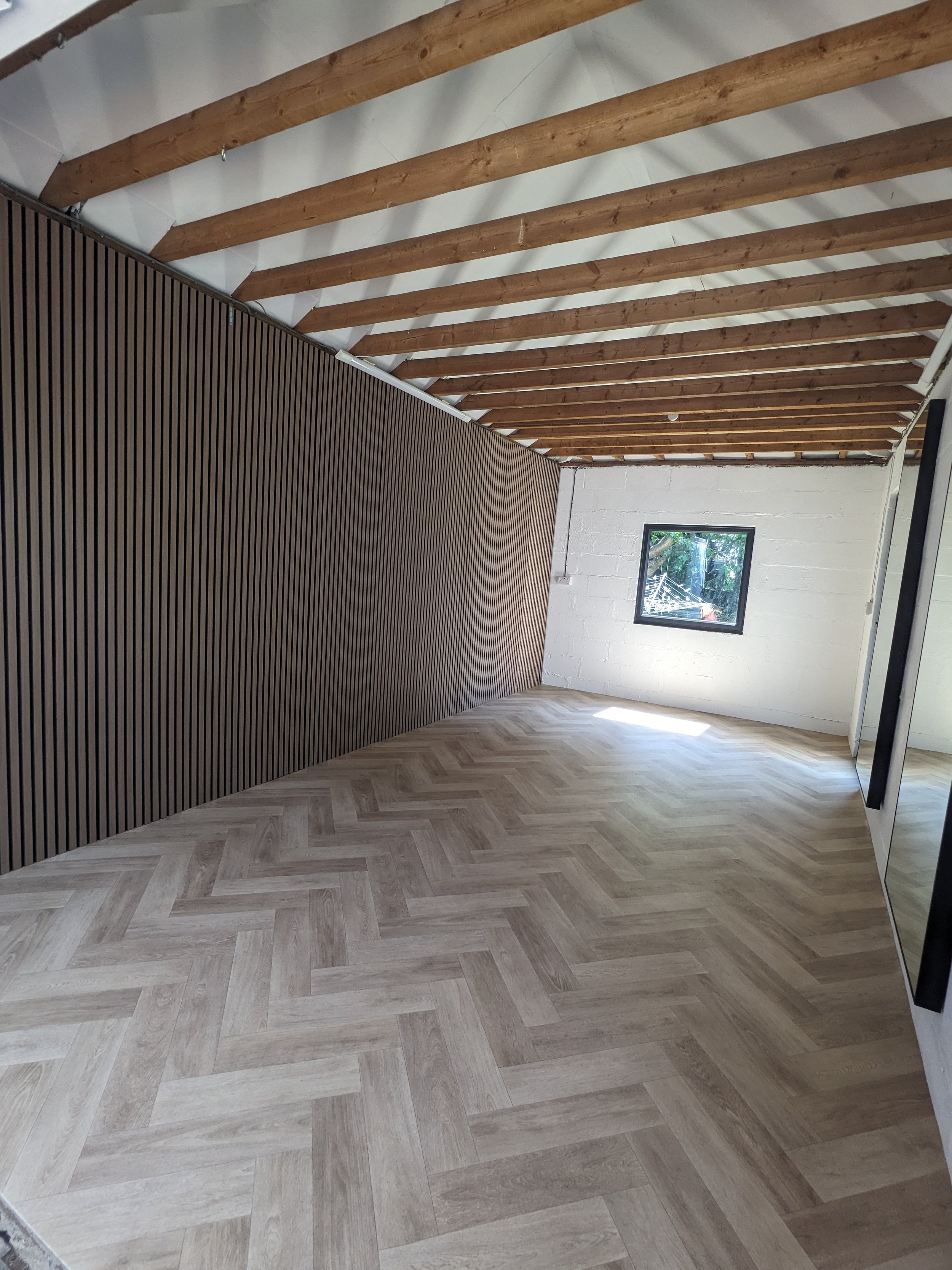 Refurbished garage gym room with wood laminate flooring, a small window, and exposed wooden ceiling beams.