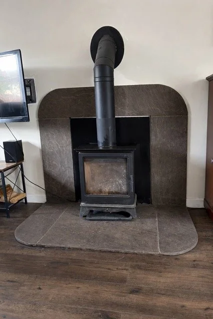 Black wood stove with a chimney pipe against a wall, set in a tiled hearth area.