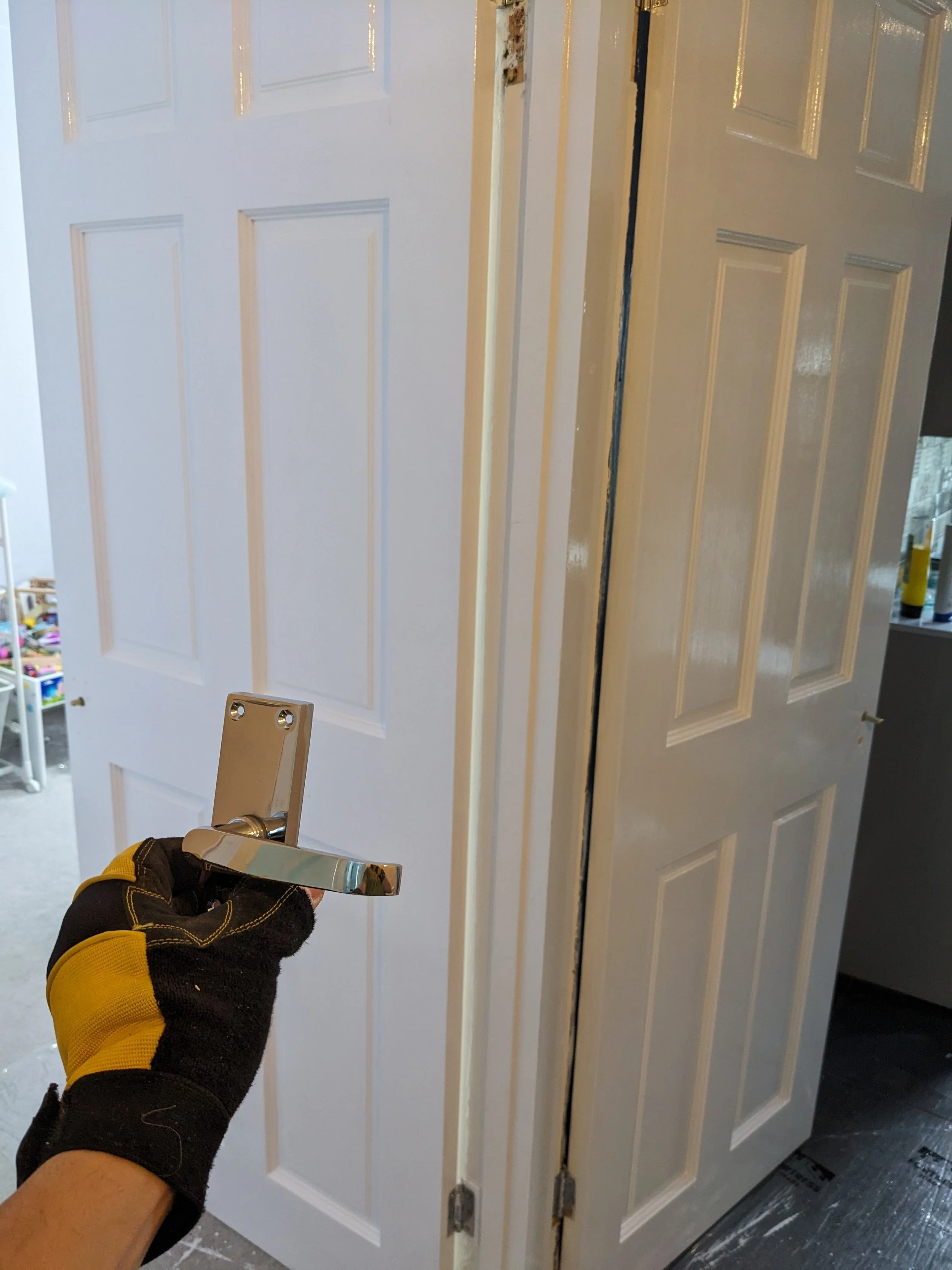 A person wearing a black and yellow work glove holding a metal door handle near a partially installed closet door.