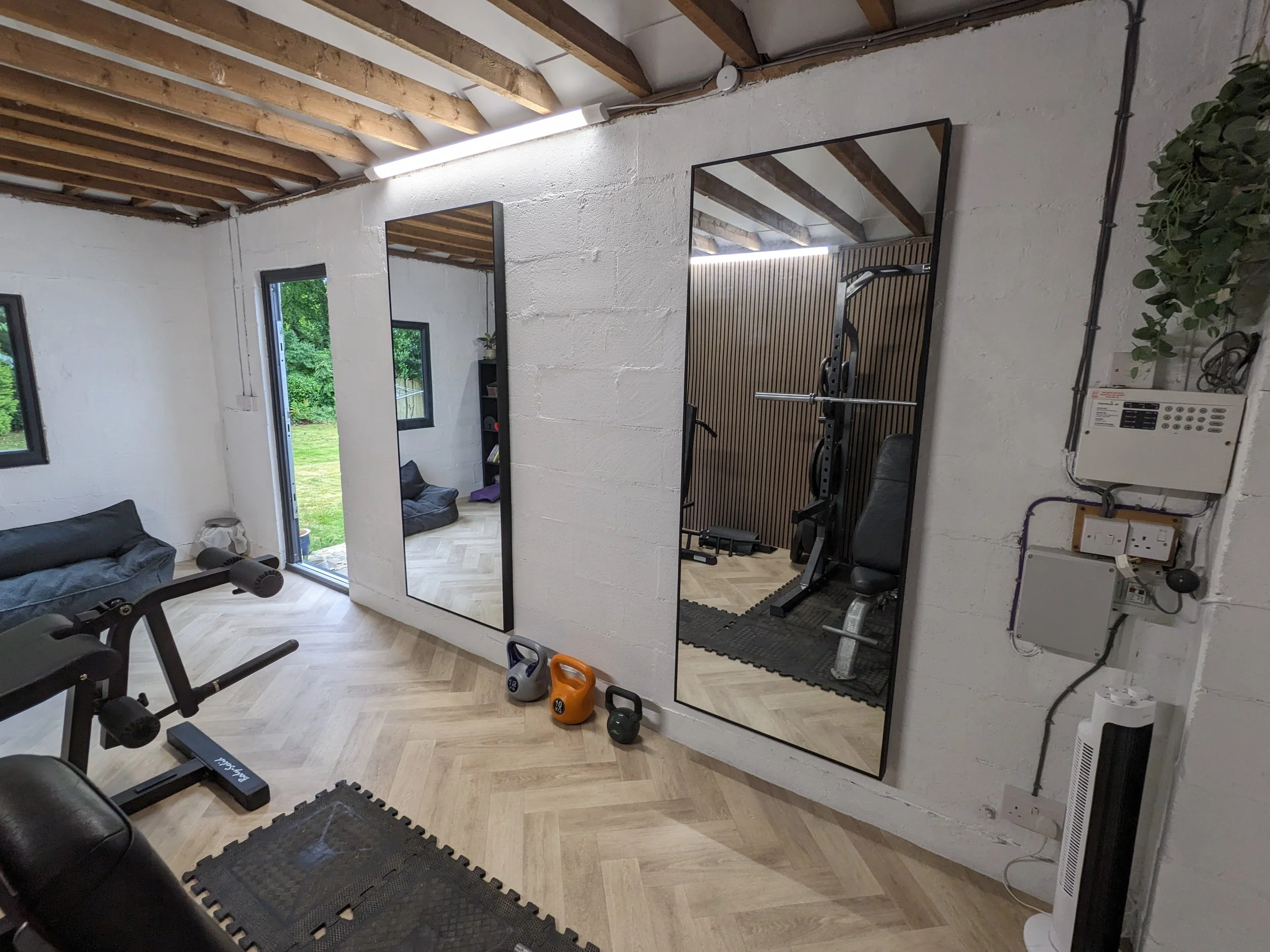 Interior of a new home gym with workout equipment, large mirrors on the wall, windows and door leading outside, and a wall-mounted control panel.