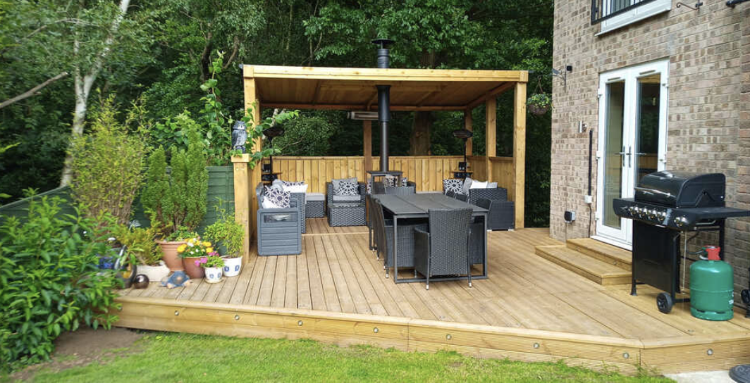 Wooden backyard deck with outdoor furniture, a grill, and a covered outdoor seating area adjacent to a brick house.