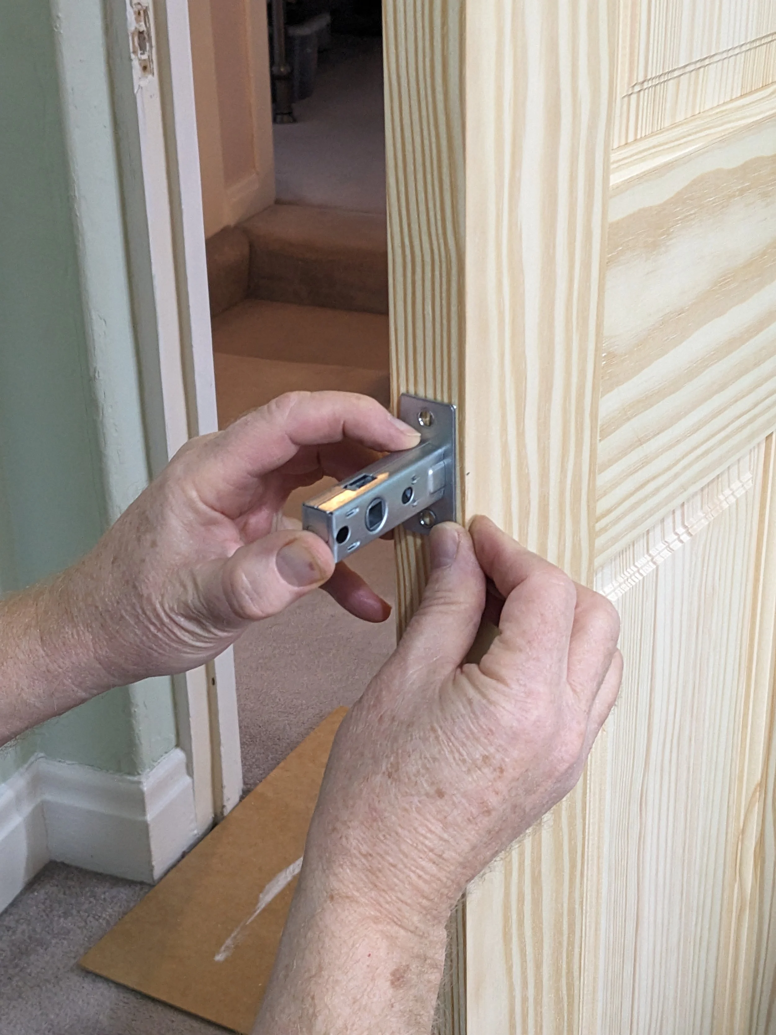 Hands installing a latch lock on a wooden door in a home.