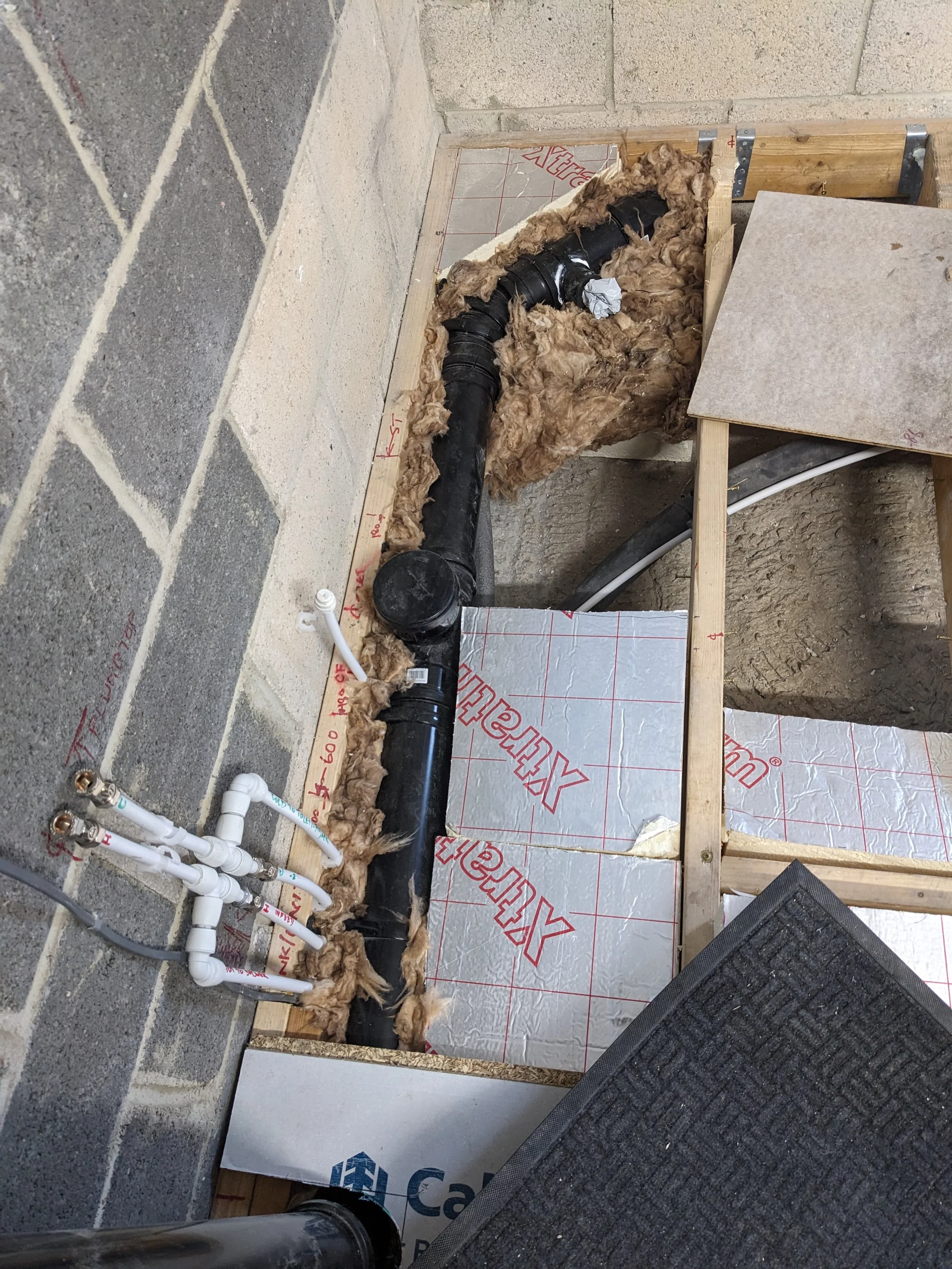 Plumbing layout with black pipe, white PVC fittings, insulation, and wooden framing for a plumbing installation.