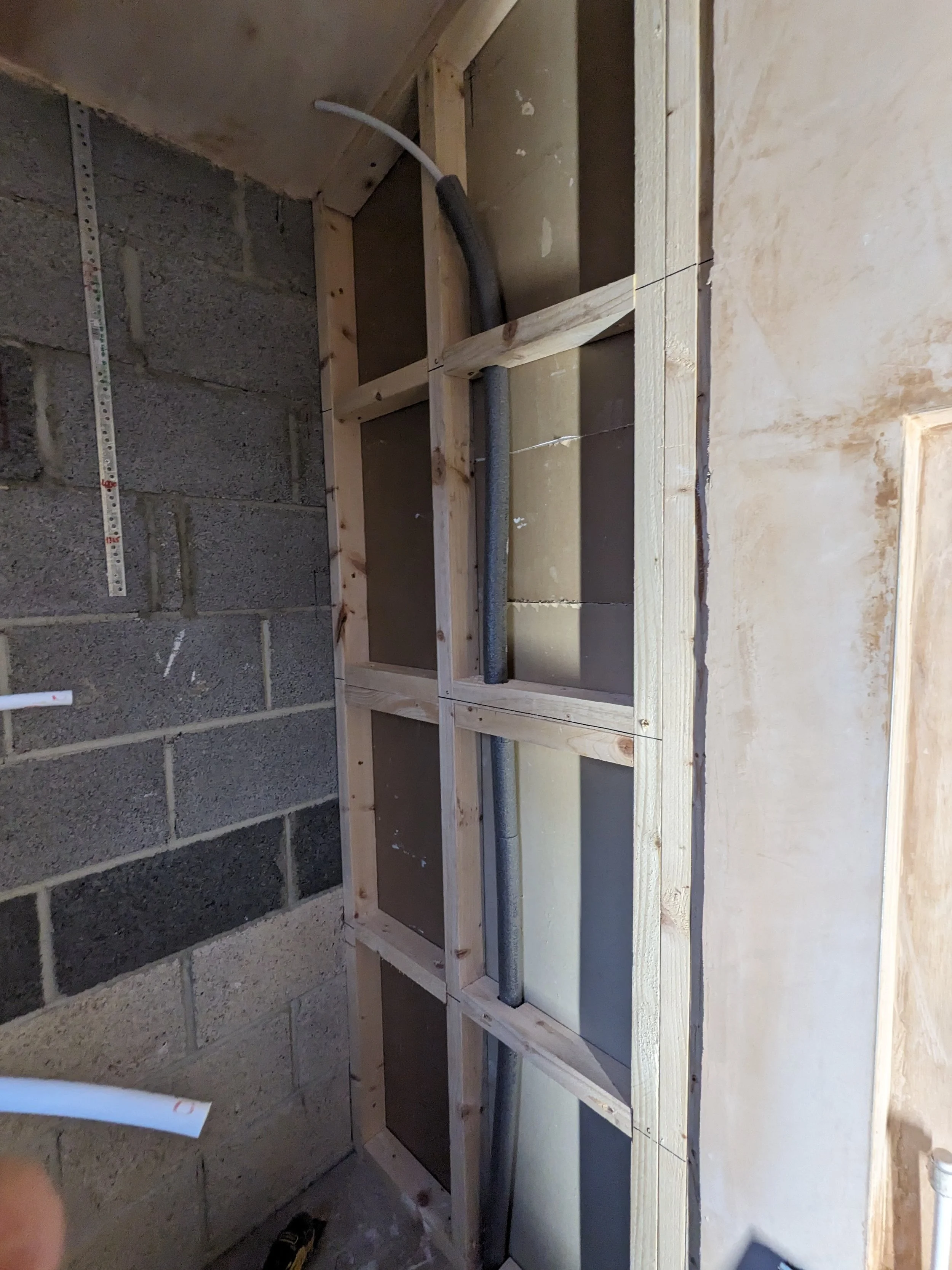Interior wall with wooden framing, electrical conduit, and cinder block wall.