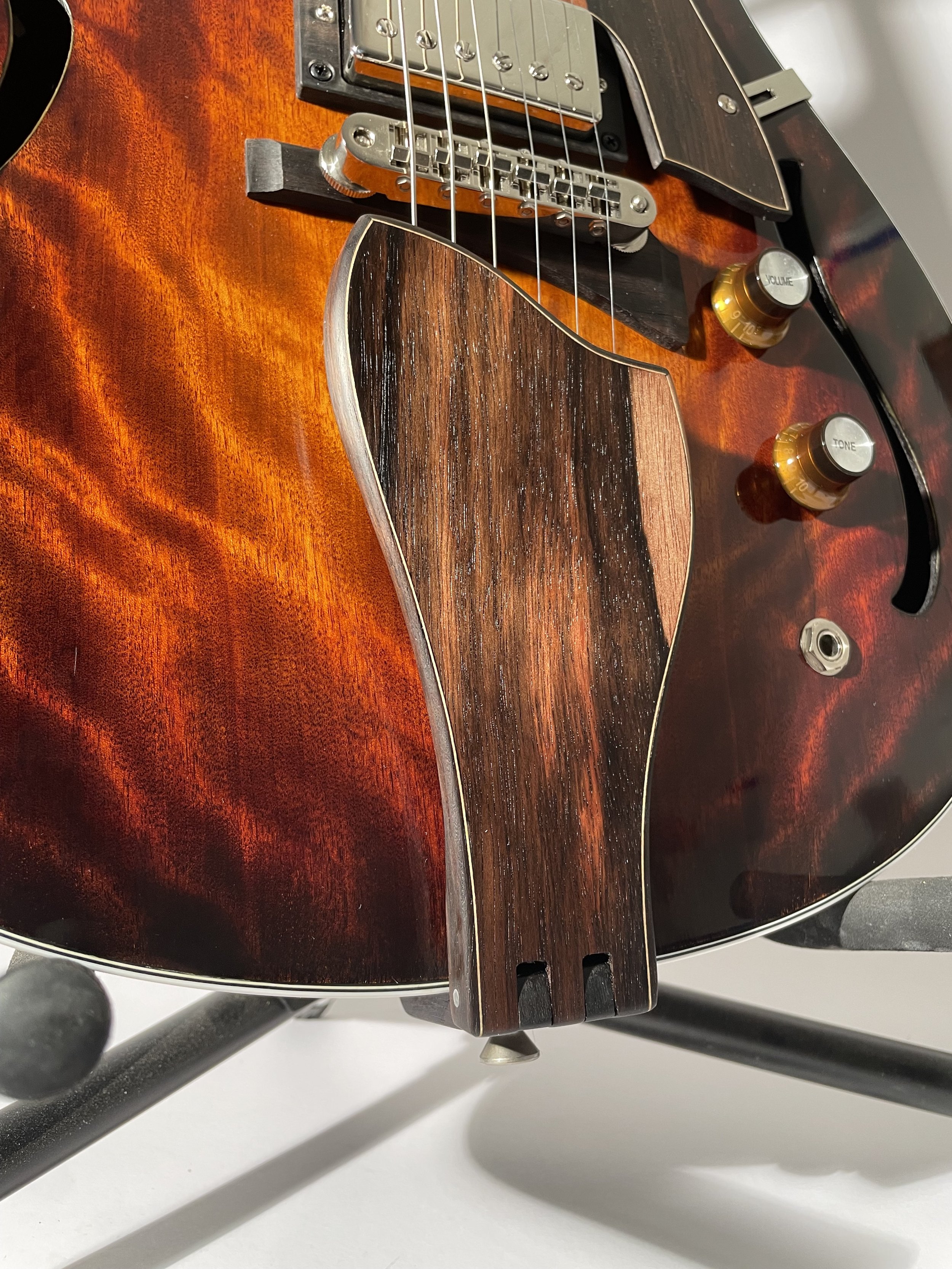 Close-up of a semi-hollow electric guitar tailpiece and body, showcasing wood grain and steel strings.