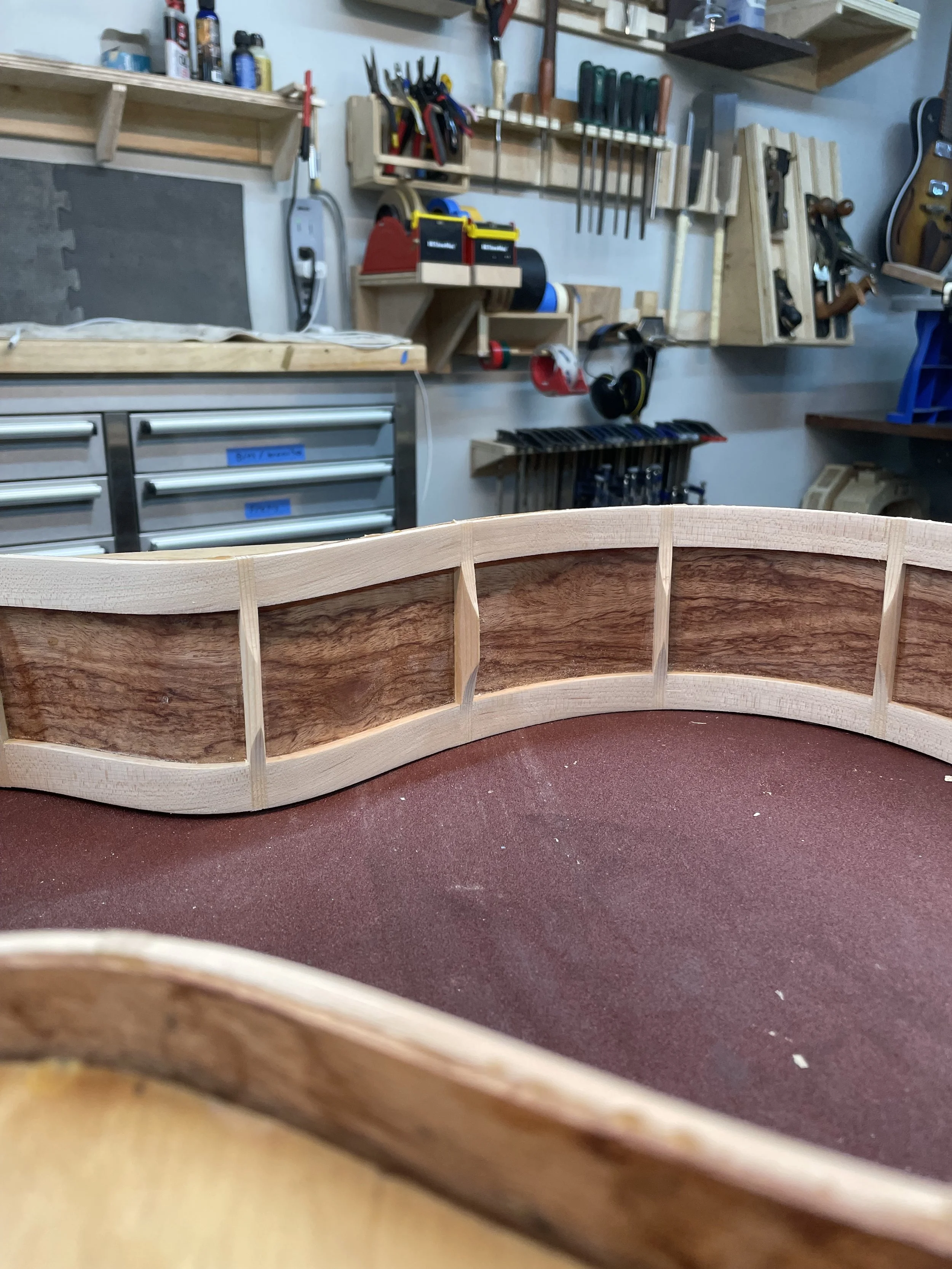 Inside view of acoustic guitar under construction in a workshop with tools on the wall.