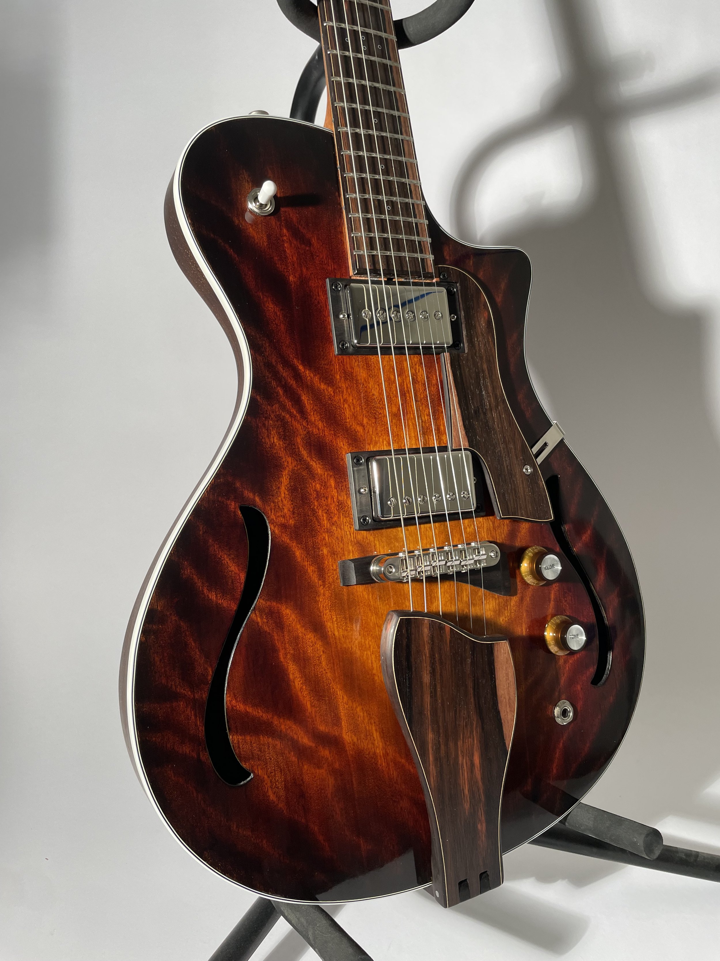 A hollow-body electric guitar with a sunburst finish and f-holes, sitting on a stand.