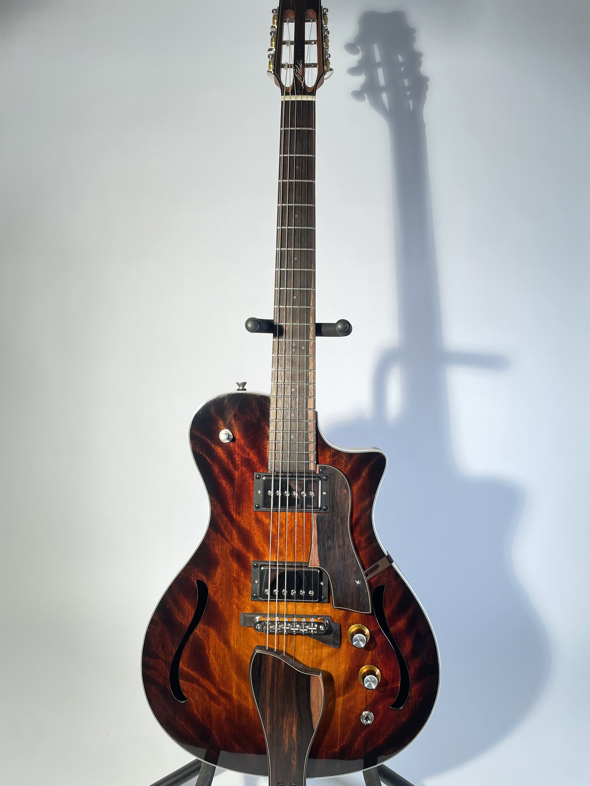 Electric guitar with f-holes and a sunburst finish on a stand, shadow cast on a light background.