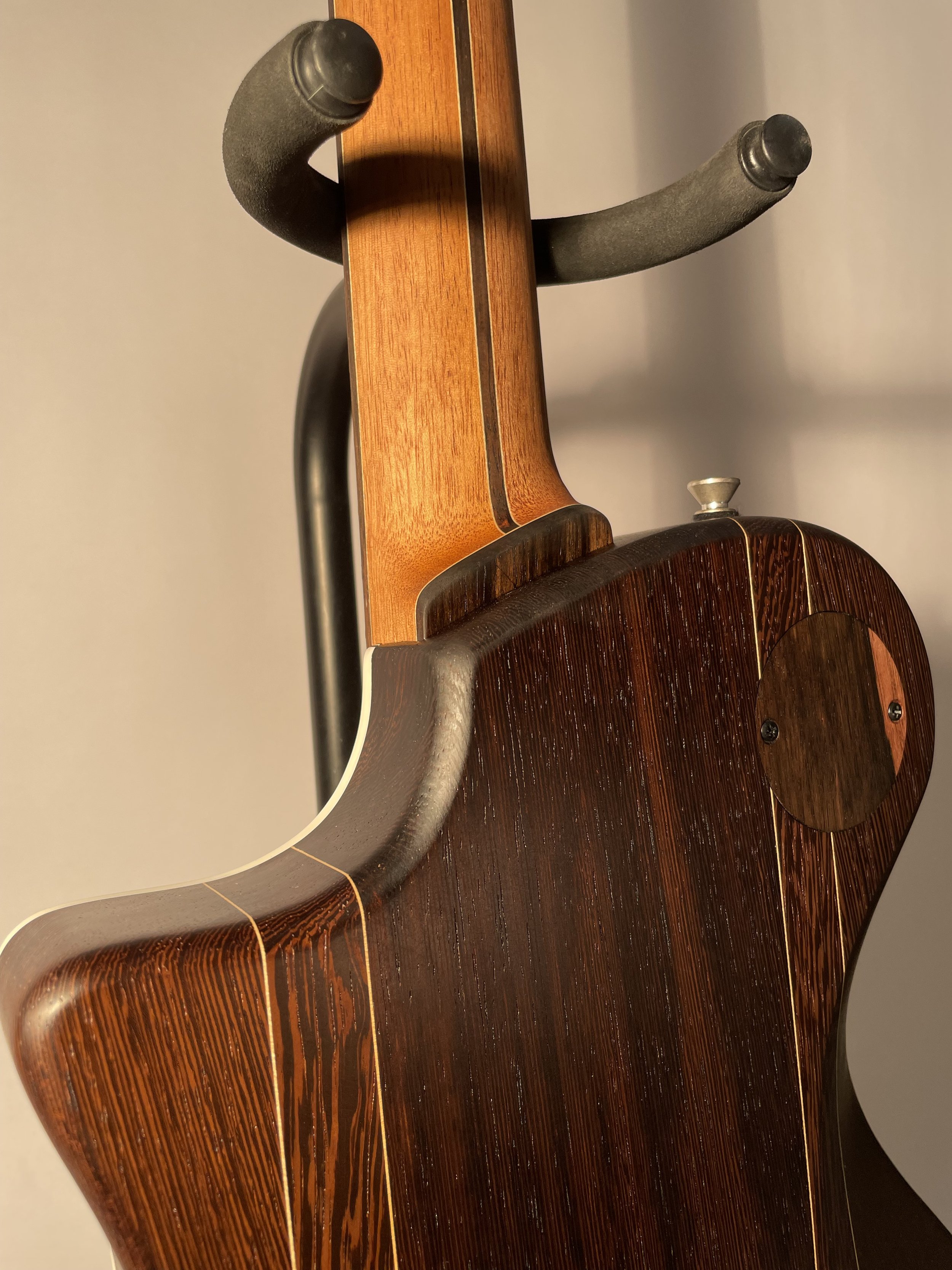 Close-up of a guitar's back and neck with a wooden finish, on a guitar stand.