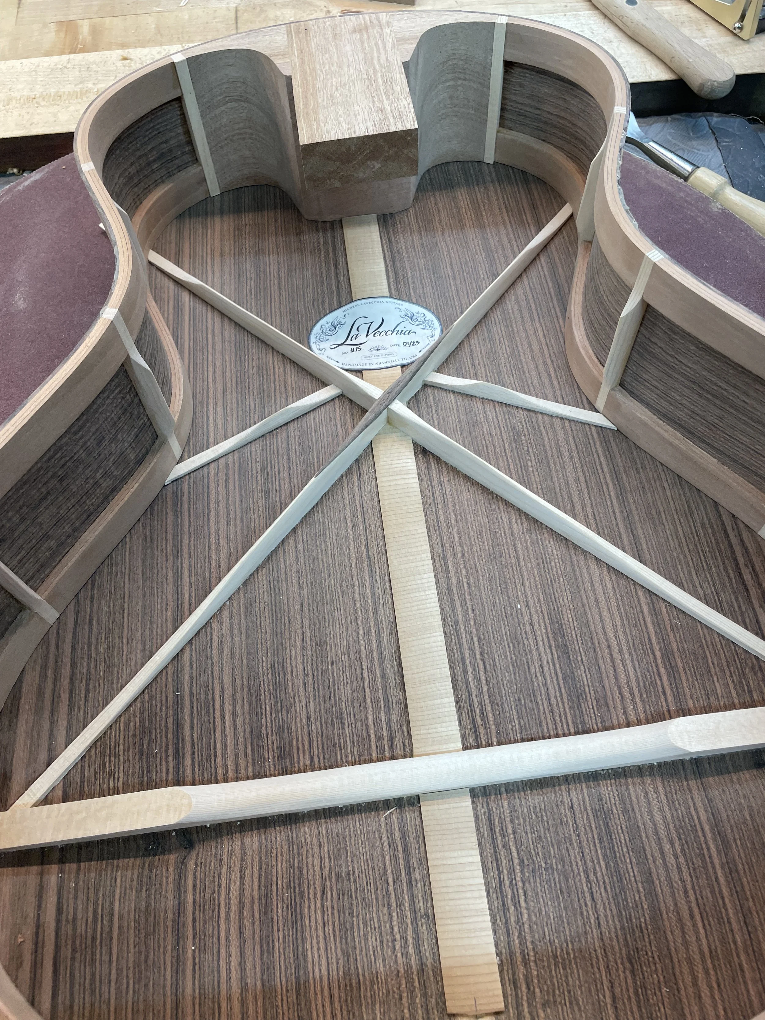Interior view of an acoustic guitar under construction, showing wooden bracing and label.