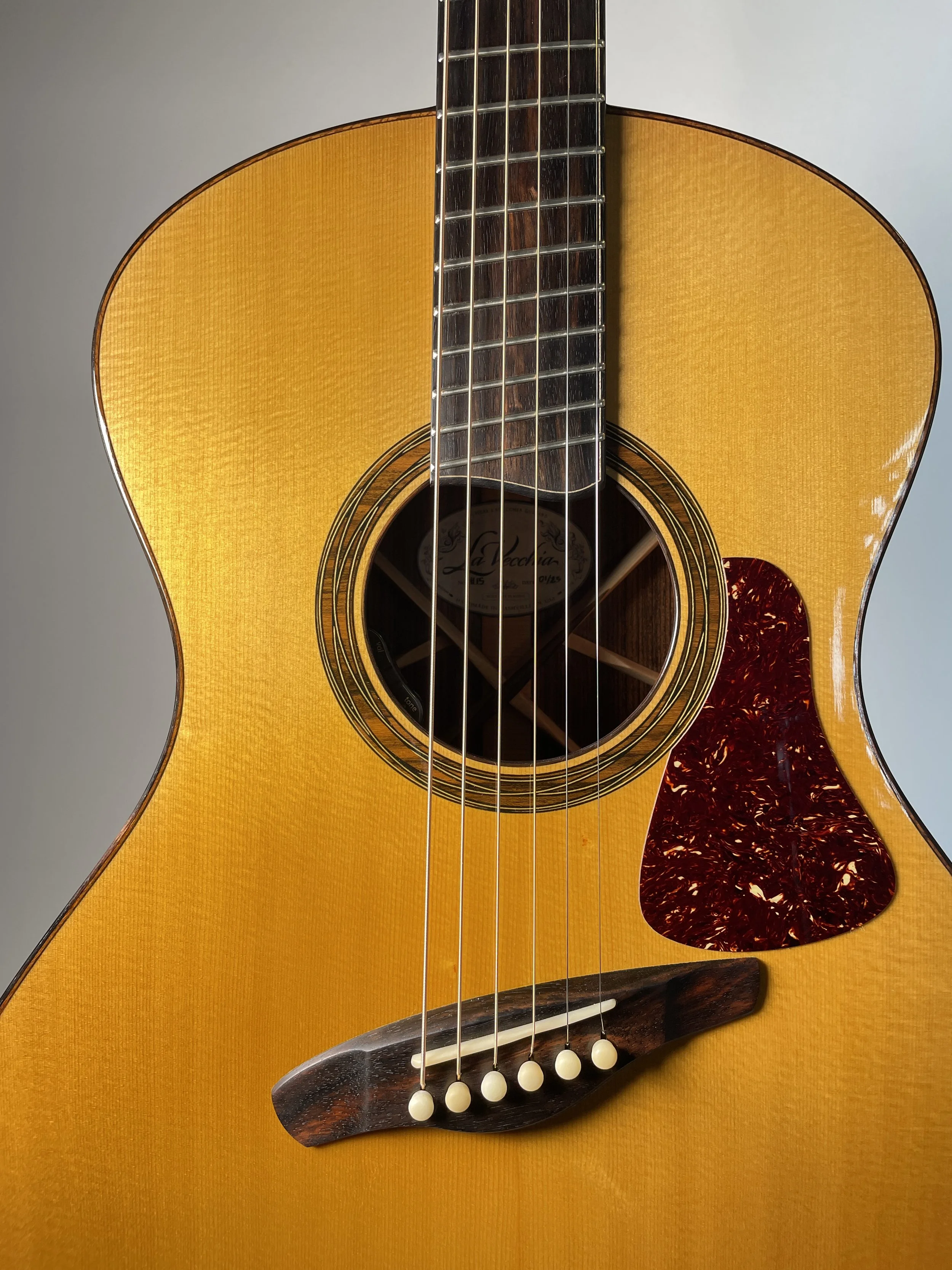 Close-up of an acoustic guitar body with a tortoiseshell pickguard and six strings.