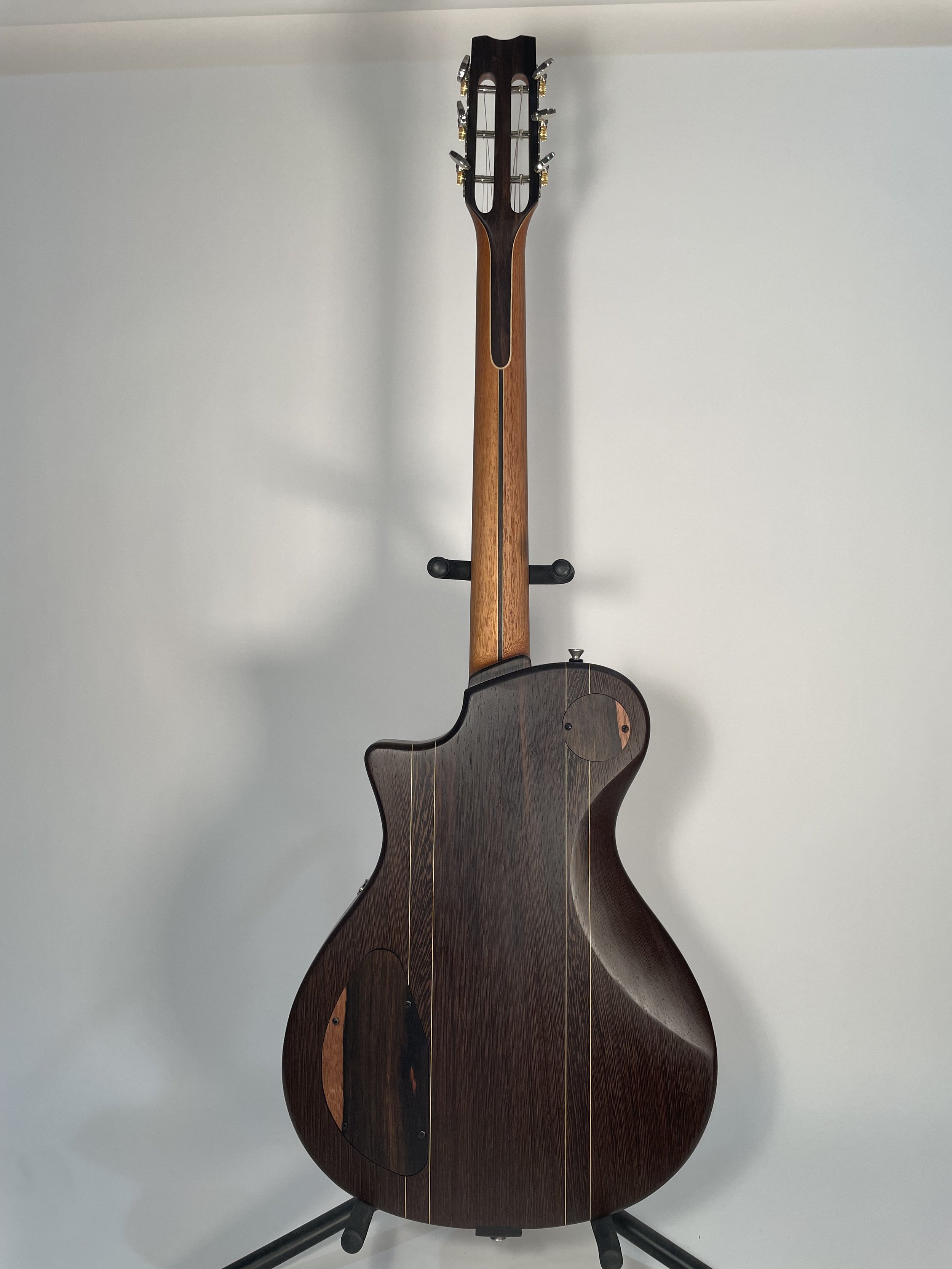 Back view of a dark wood acoustic guitar on a stand against a white background.